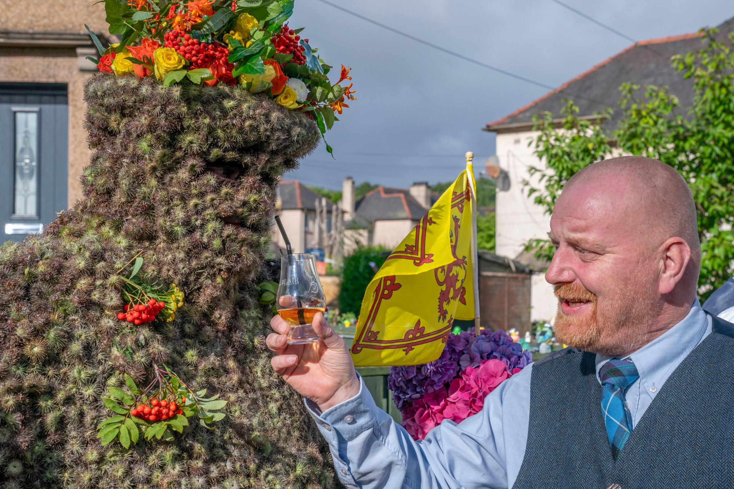 Burryman being given whisky through a straw