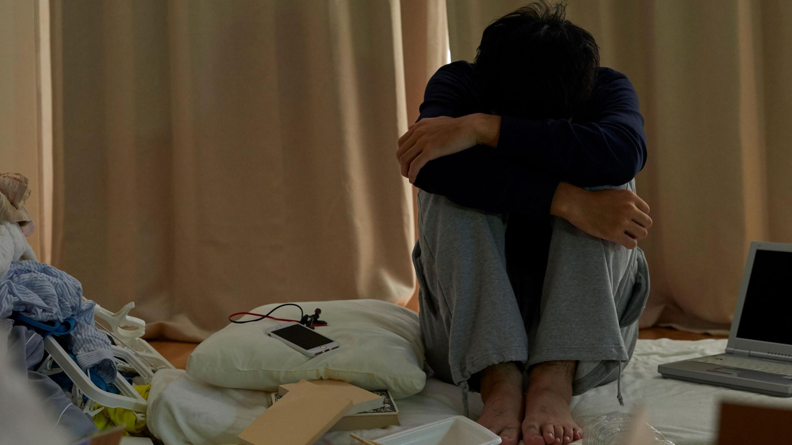 A boy sits on a bed with his head in his knees