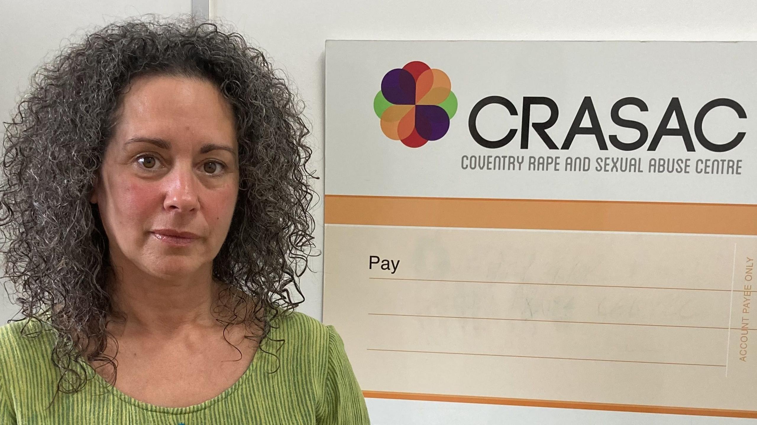 Natalie is wearing a green top and is sitting in front of a large blank display cheque which says CRASAC