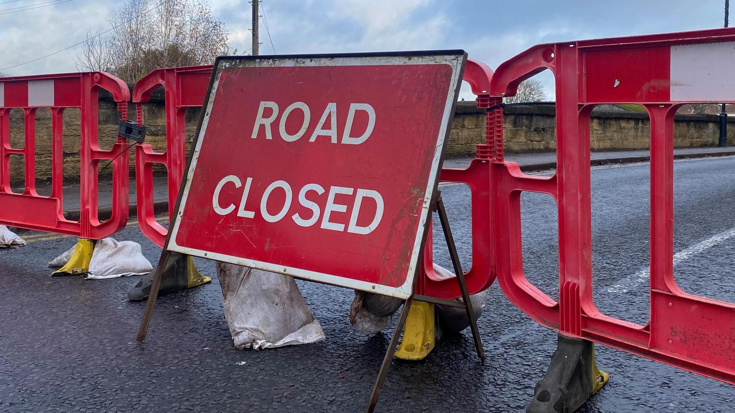 A "road closed" sign is standing in front of red plastic barriers on a road bridge.