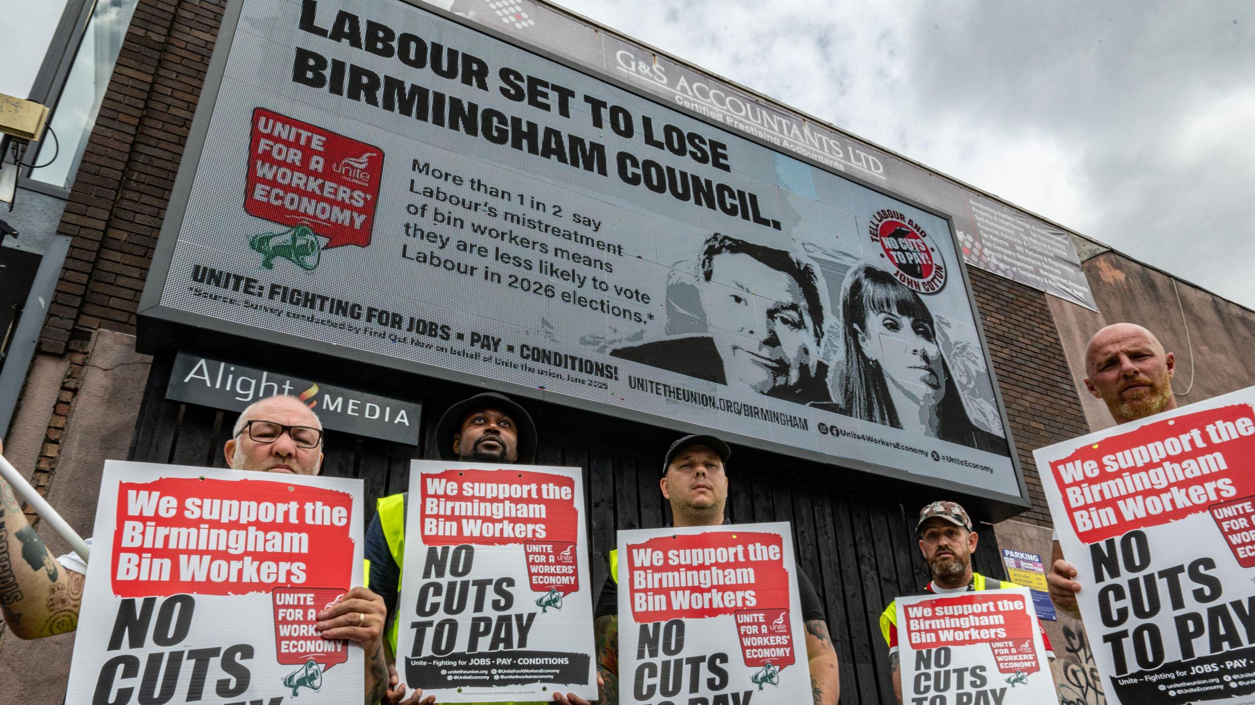 Striking bin workers stand in front of billboards commissioned by the Unite trade union, holding placards in support of striking bin workers
