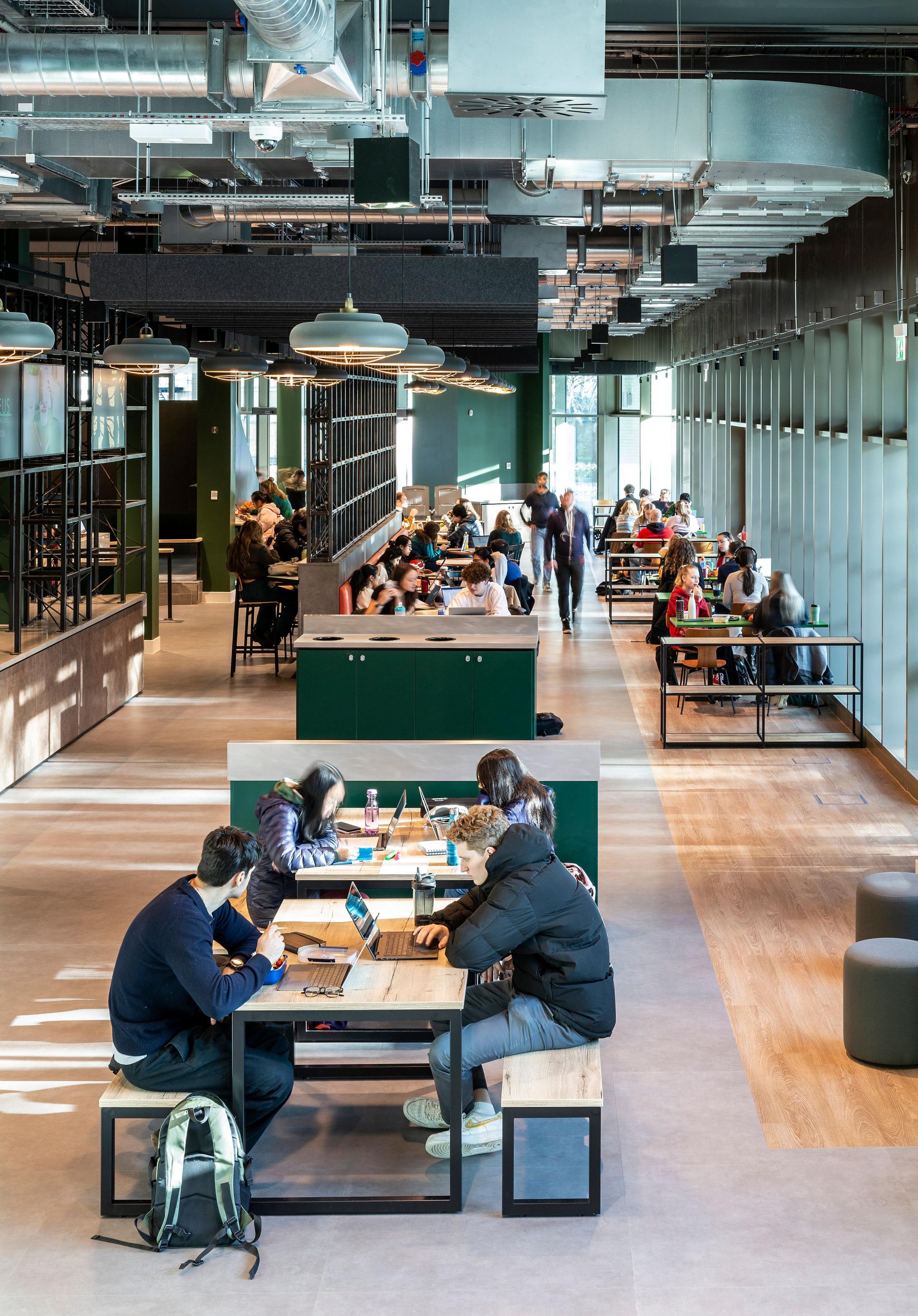 An area of the Nucleus showing a bright airy space with big tables and seating for groups to sit and work. Wooden floors, high ceilings, modern lighting and green soft furnishings make it a modern attractive space.