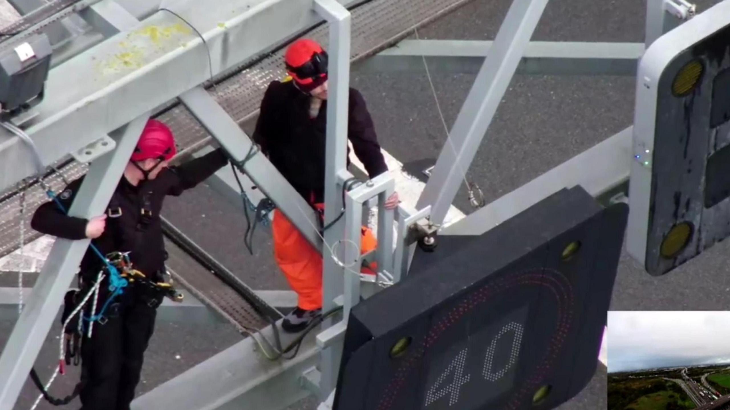 Protesters climb a sign on the M25