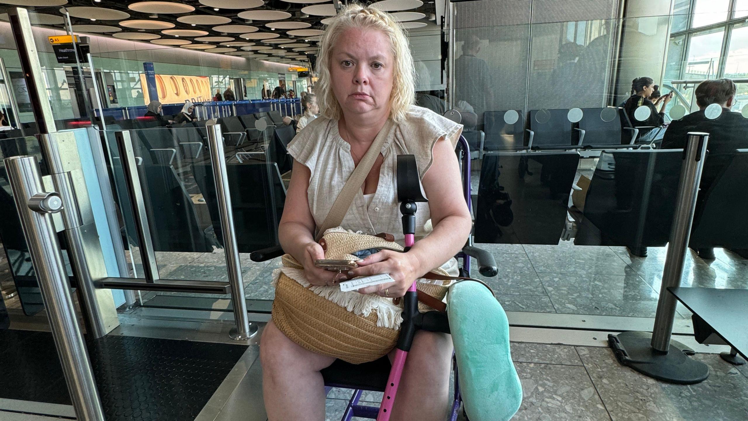 Jo Pohl with sitting at the departure gates area of Heathrow with an annoyed expression