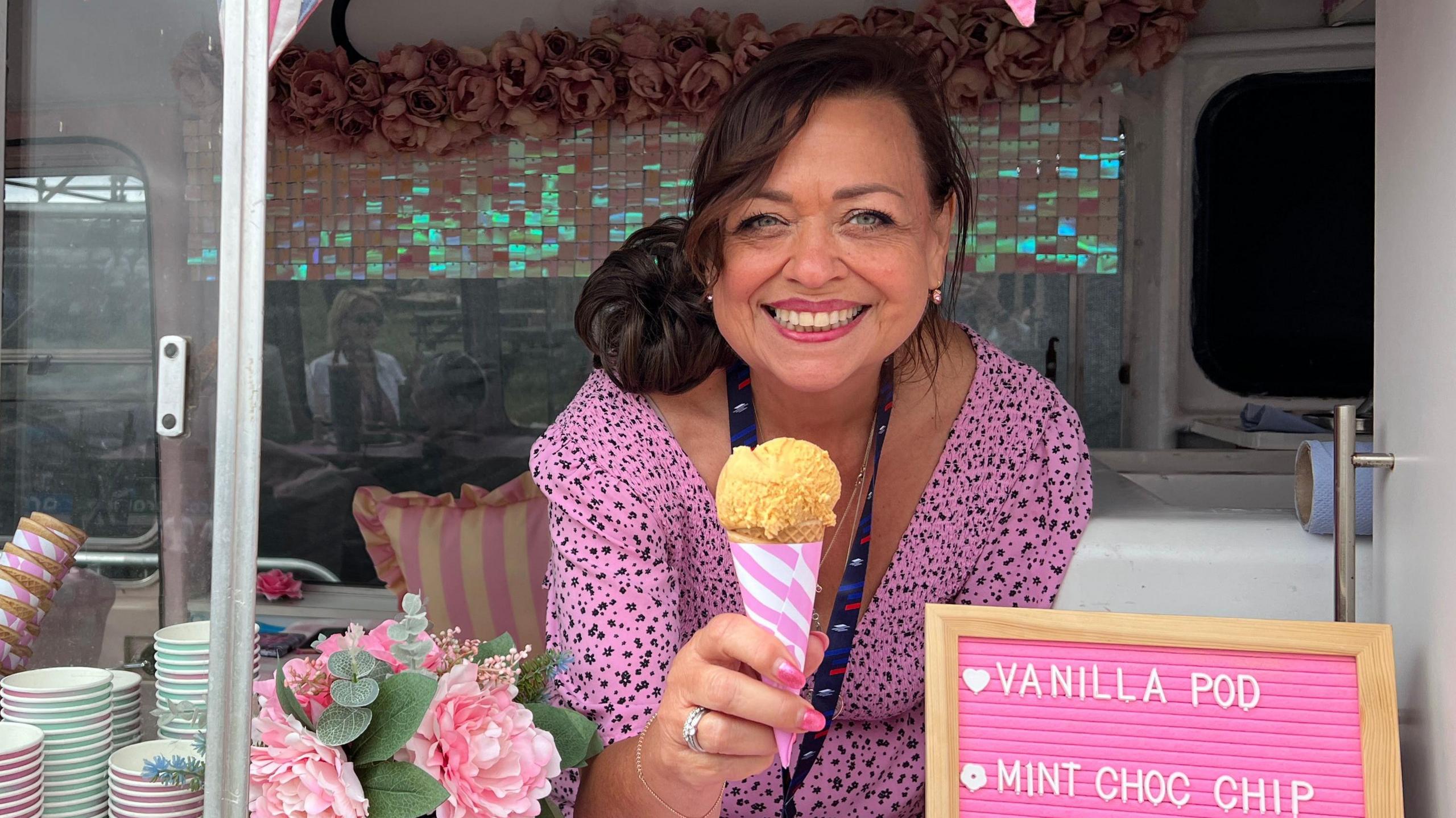 A woman in a pink leopard print dress holds an ice cream inside a vintage ice cream van