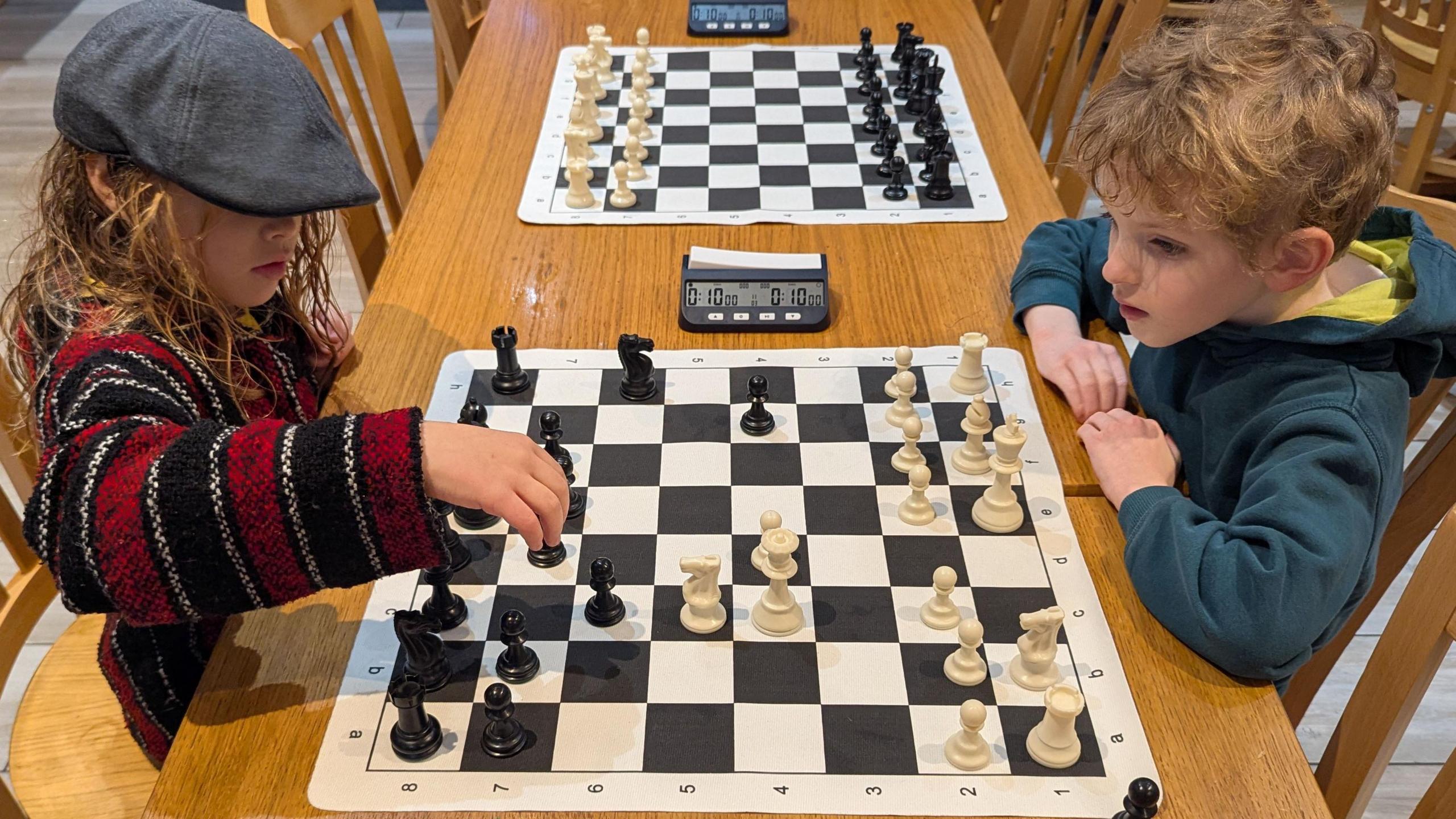 Llun yn dangos dau blentyn ifanc yn eistedd wrth fwrdd, yn chwarae gwyddbwyll.