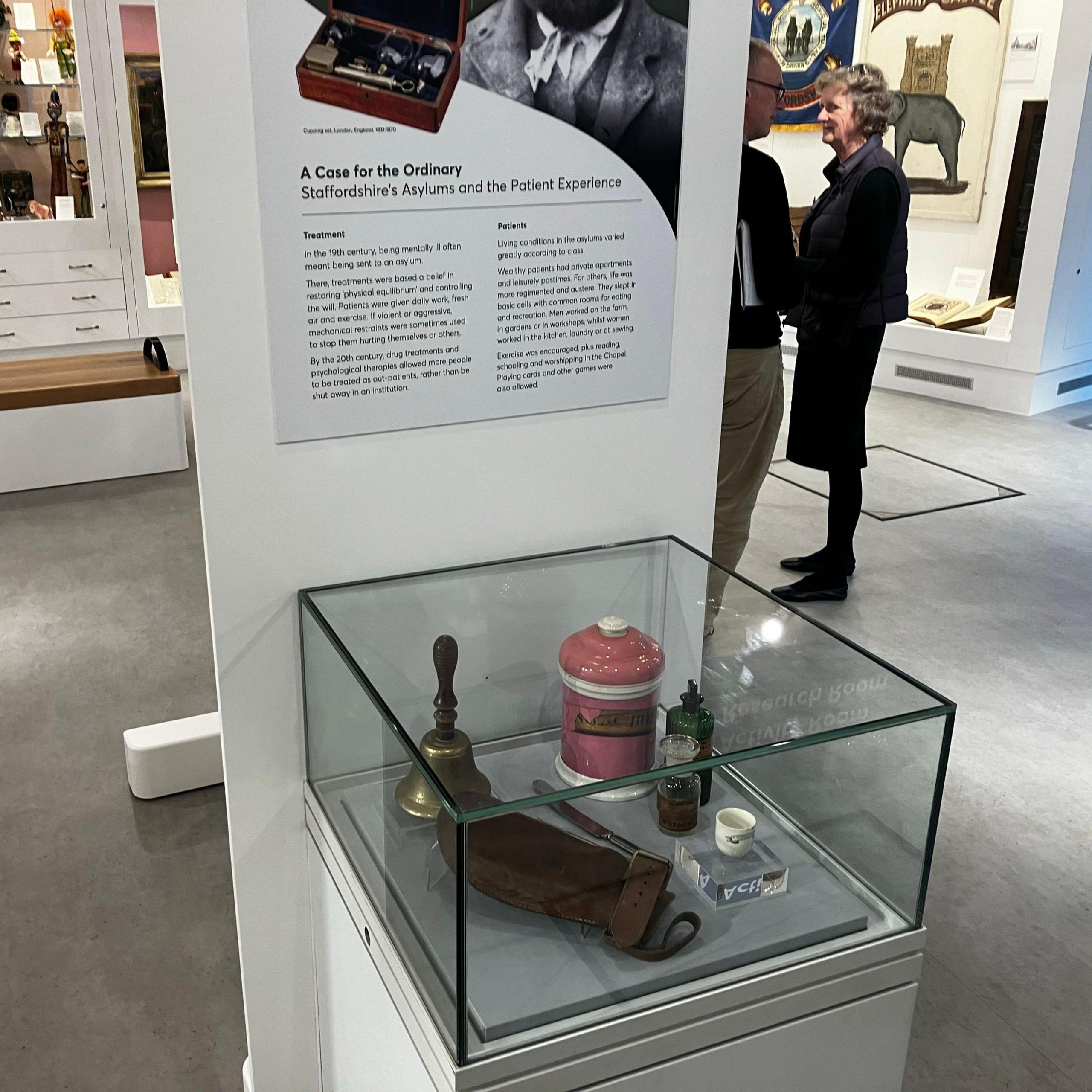 A glass display case containing various items including a school bell, with a board behind it detailing information about the historical artefacts.