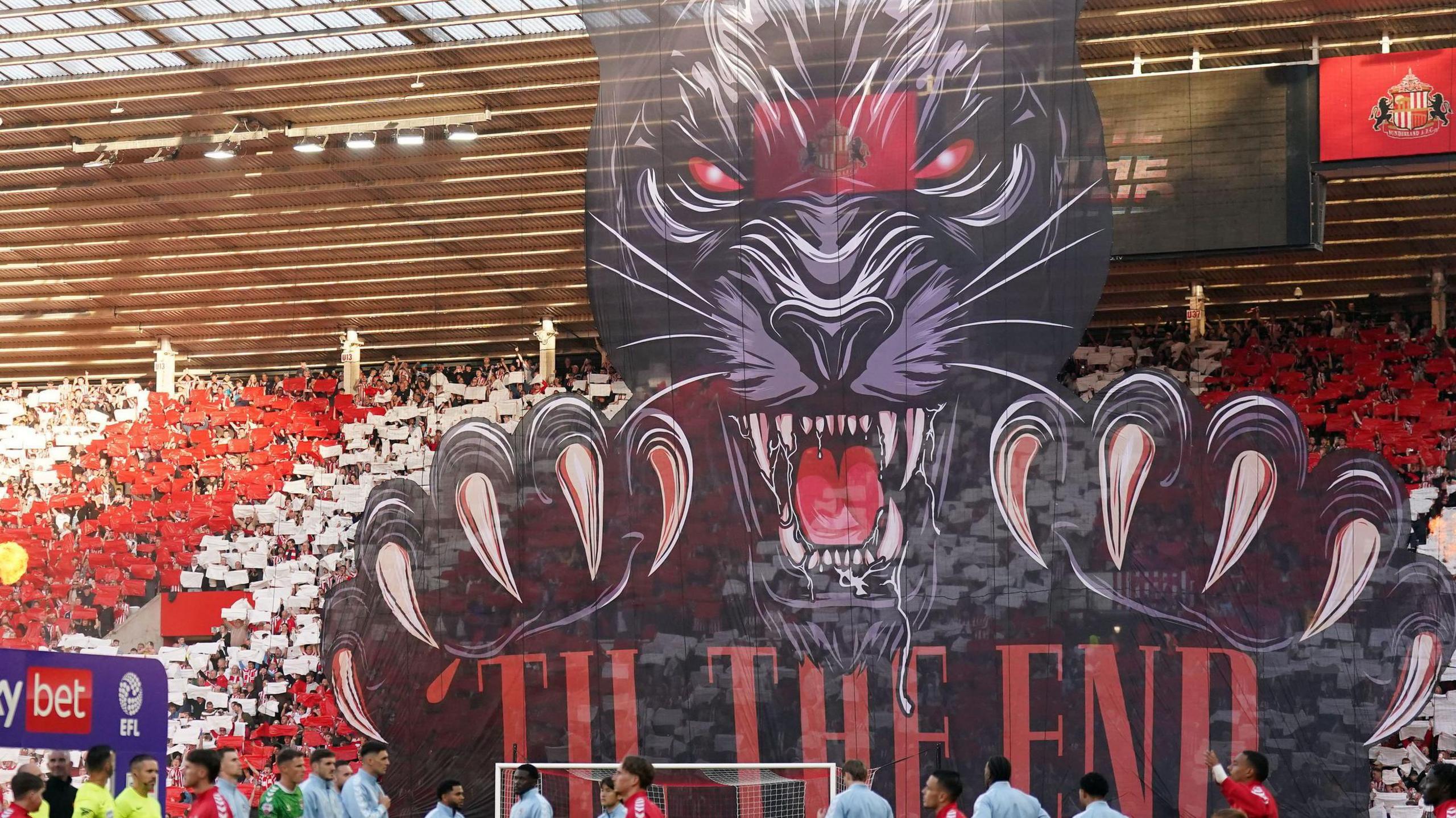 Sunderland and Coventry City players walk onto the field as a large banner is displayed before the Sky Bet Championship play off semi final, second leg match at the Stadium of Light, Sunderland. The banner depicts a ferocious, snarling black cat with the words "'TIL THE END" underneath it.