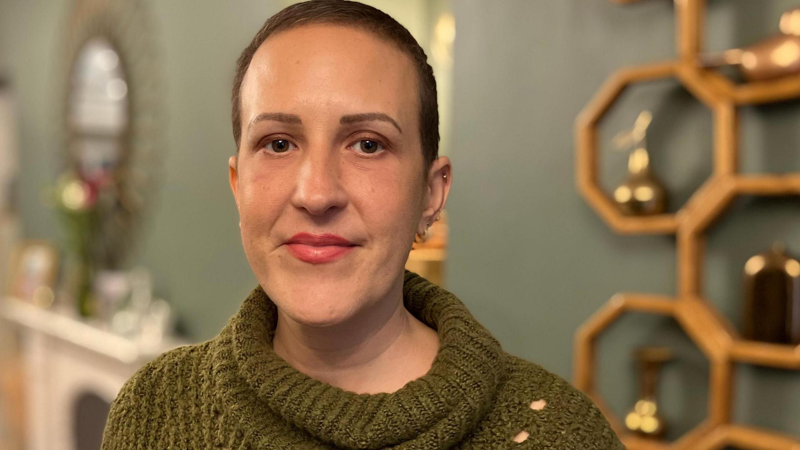 Rachel Davies standing in her living room during her campaign to make the life-extending drug Enhertu to be made available through the NHS in Wales. She is wearing a green jumper, and facing the camera.