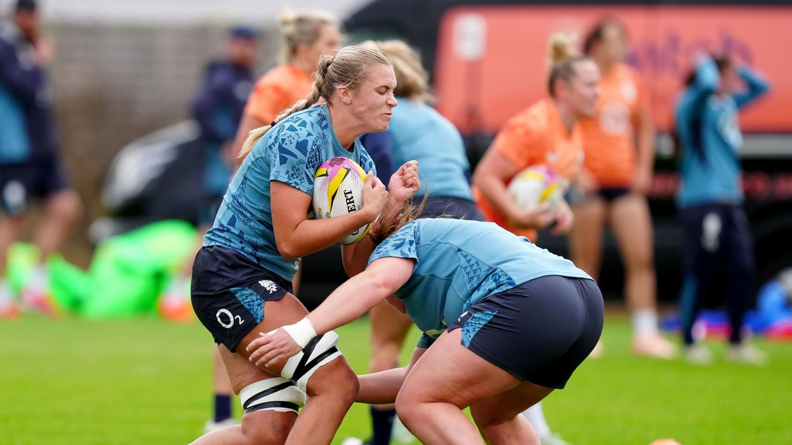 Two England's women rugby players, wearing light blue tops and dark shorts, clash as one tackles the other as she runs with the ball during a training session in Bristol.