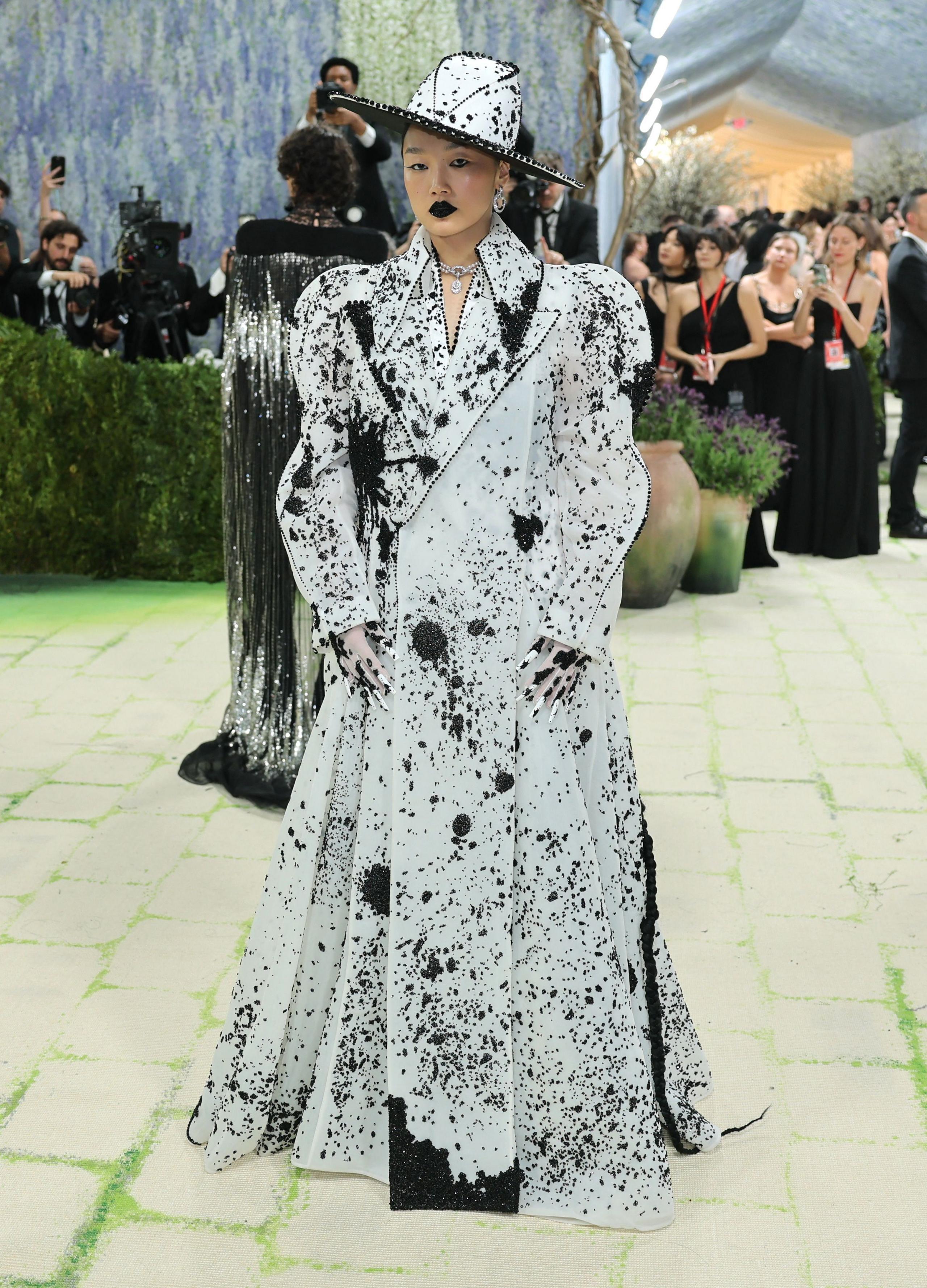 Audrey Nuna poses during the Met Gala wearing a long white coat and hat with splashes of black paint. 