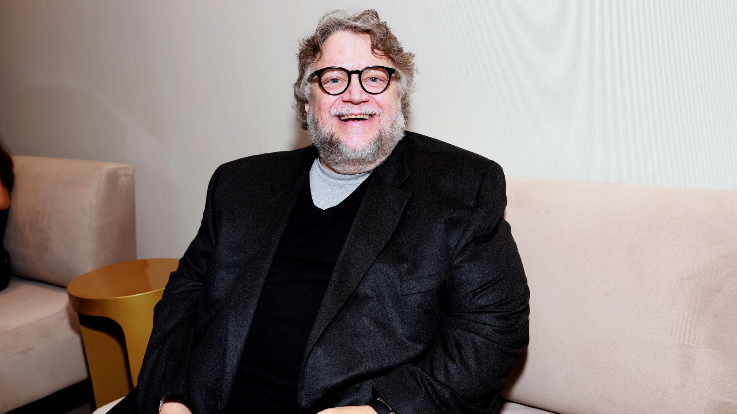 Film director Guillermo del Toro smiling at the camera while sitting on a couch