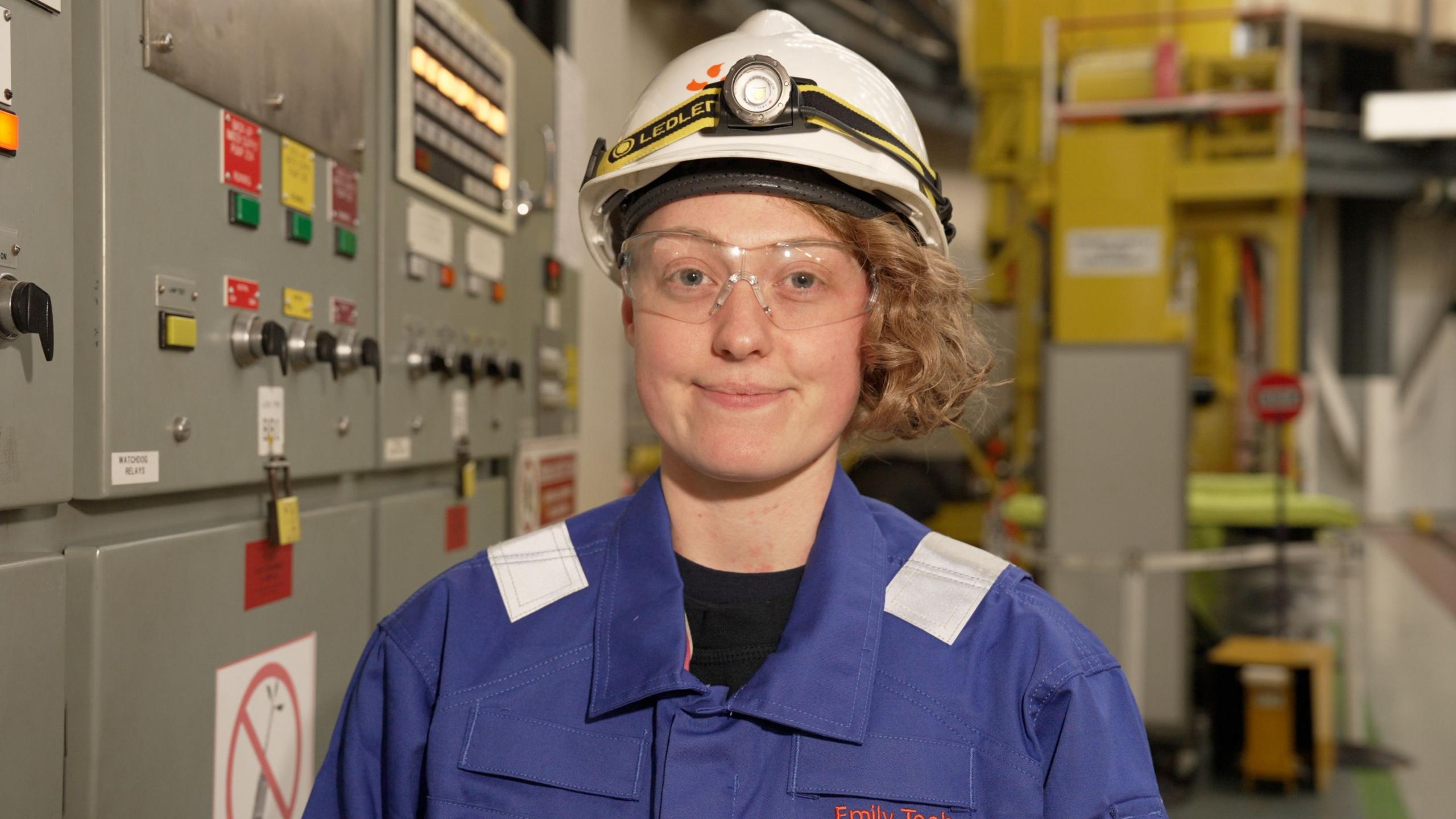 Emily Teehan - a woman in a blue work suit with a white hard hat.