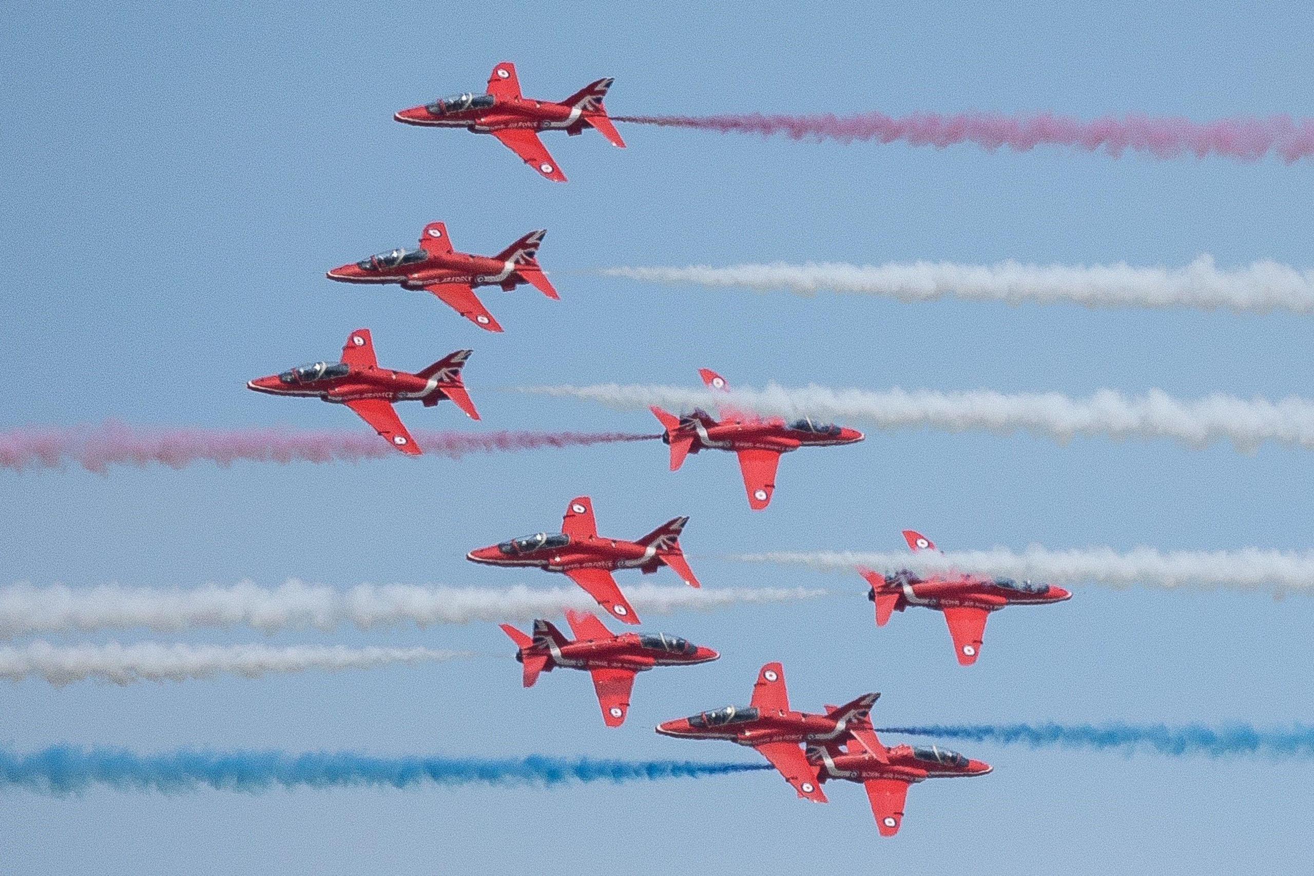 There are nine Red Arrows in the picture, some are pointing in different directions. There are red, white and blue smoke trails.