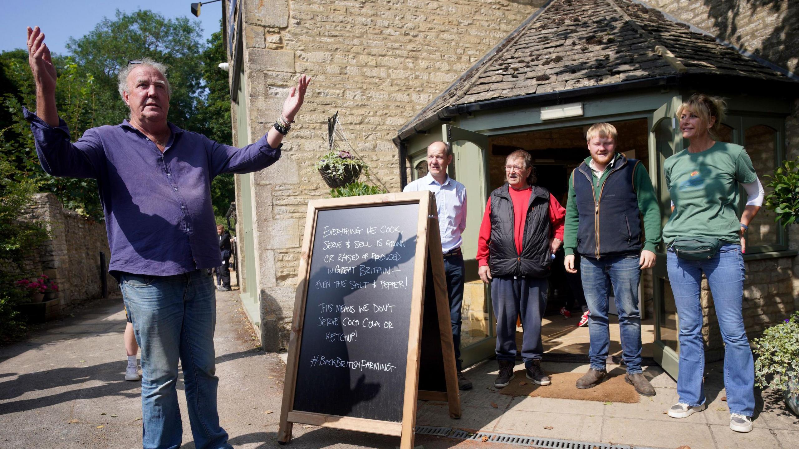 Jeremy Clarkson on the left outside the pub next to a blackboard sign