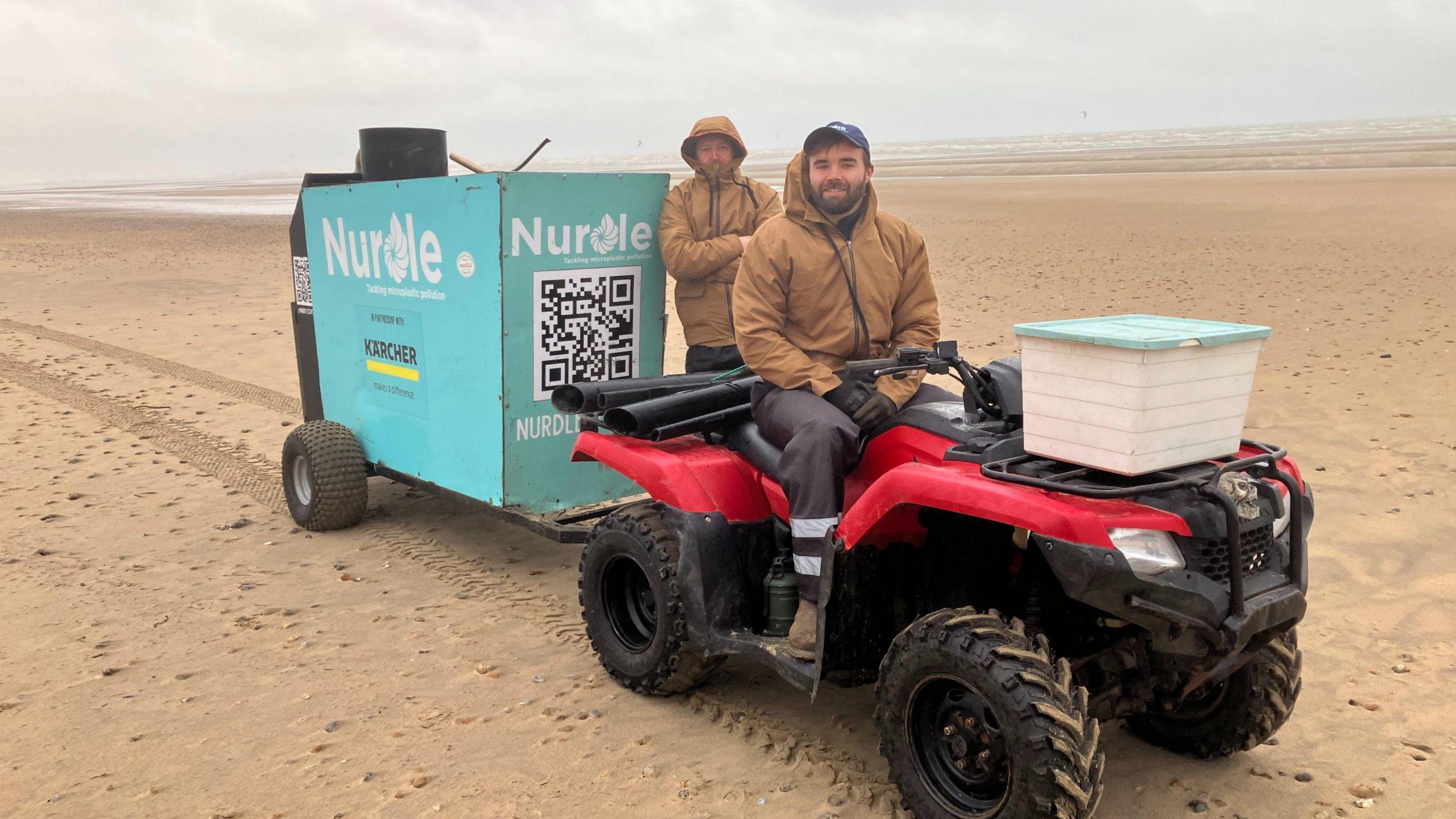 Josh Beech sits on a quad bike on Camber Sands, with Dominic Manning standing behind him.