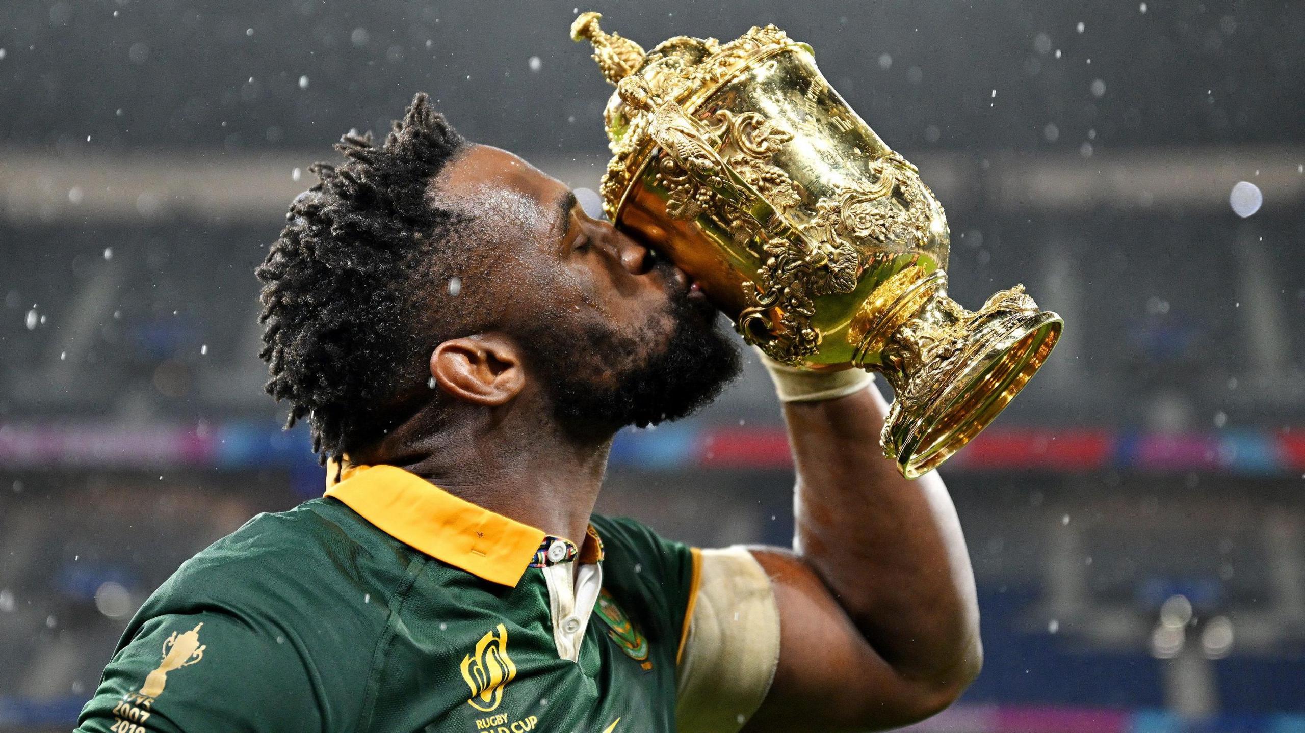 Siya Kolisi, wearing a green Springboks jersey with gold collar, kisses the Rugby World Cup trophy at the Stade de France in 2023