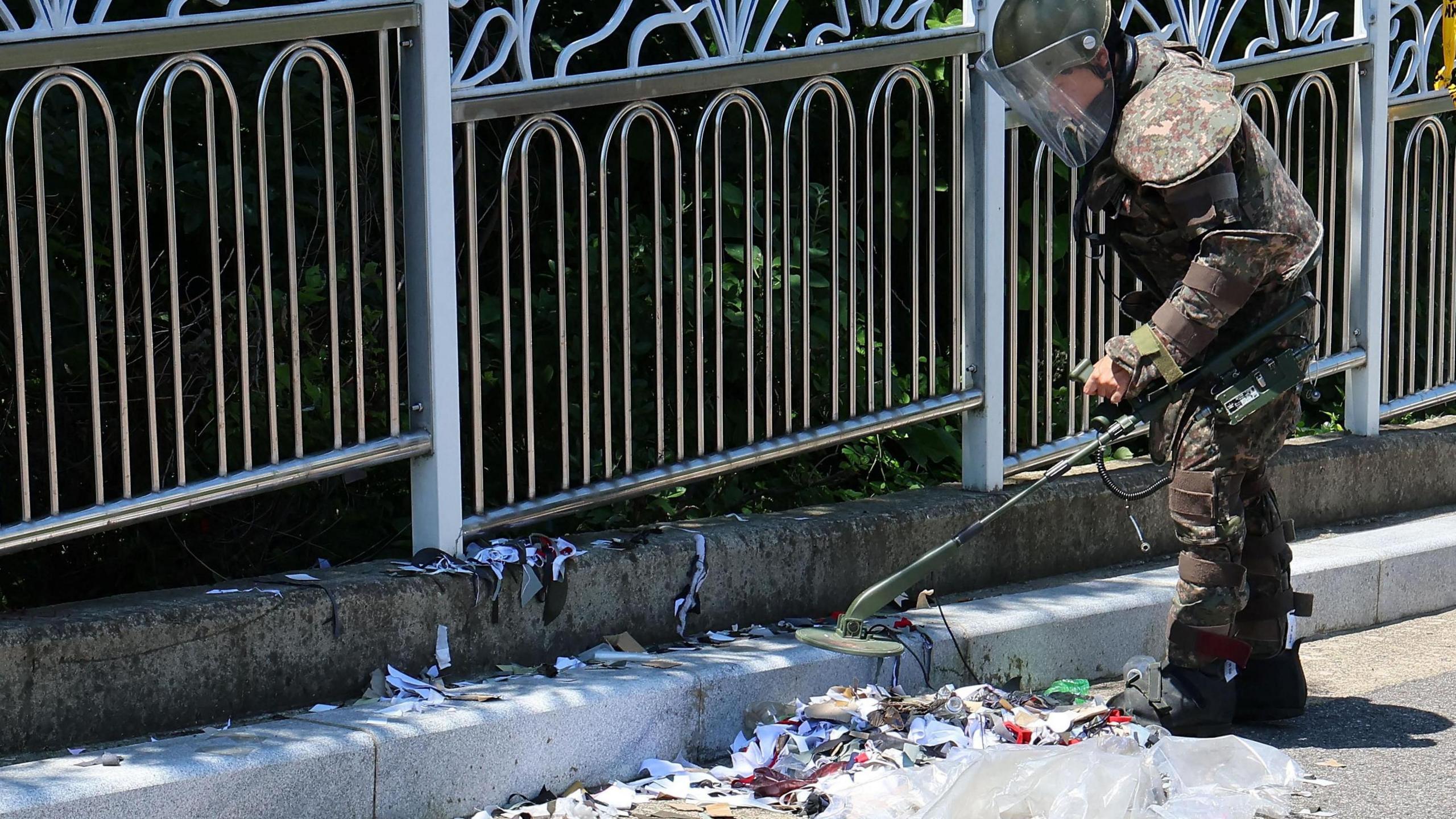 A South Korean soldier in protective equipment scans rubbish dumped by a North Korean balloon.