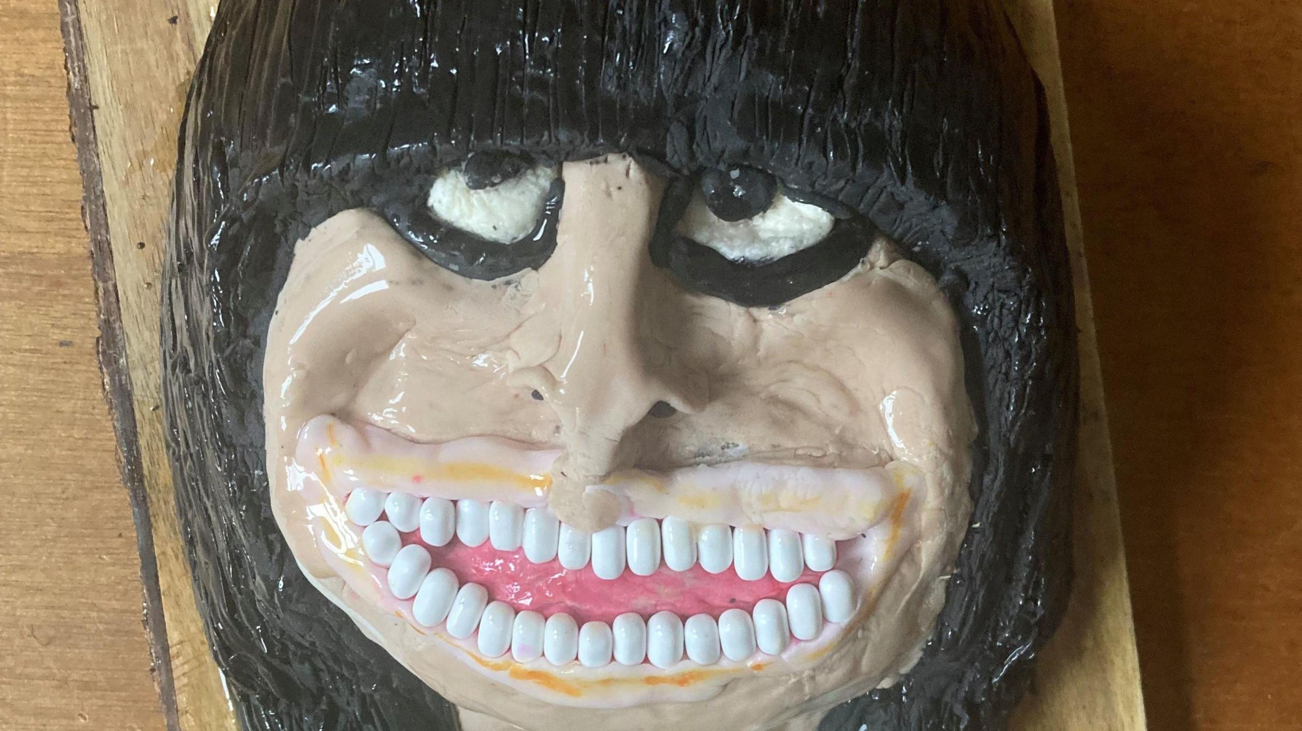 A cake of Claudia Winkleman with thick black icing for hair and multiple Tic Tacs for teeth. 