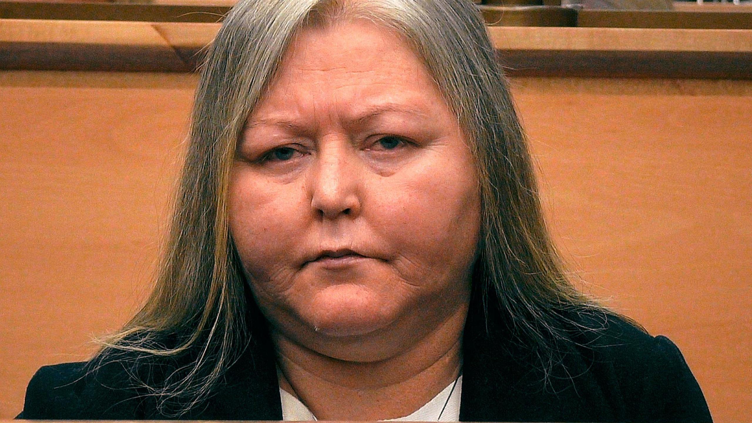 Photo of Donna Brand in court. She has long hair which is going grey and is wearing a black jacket. 