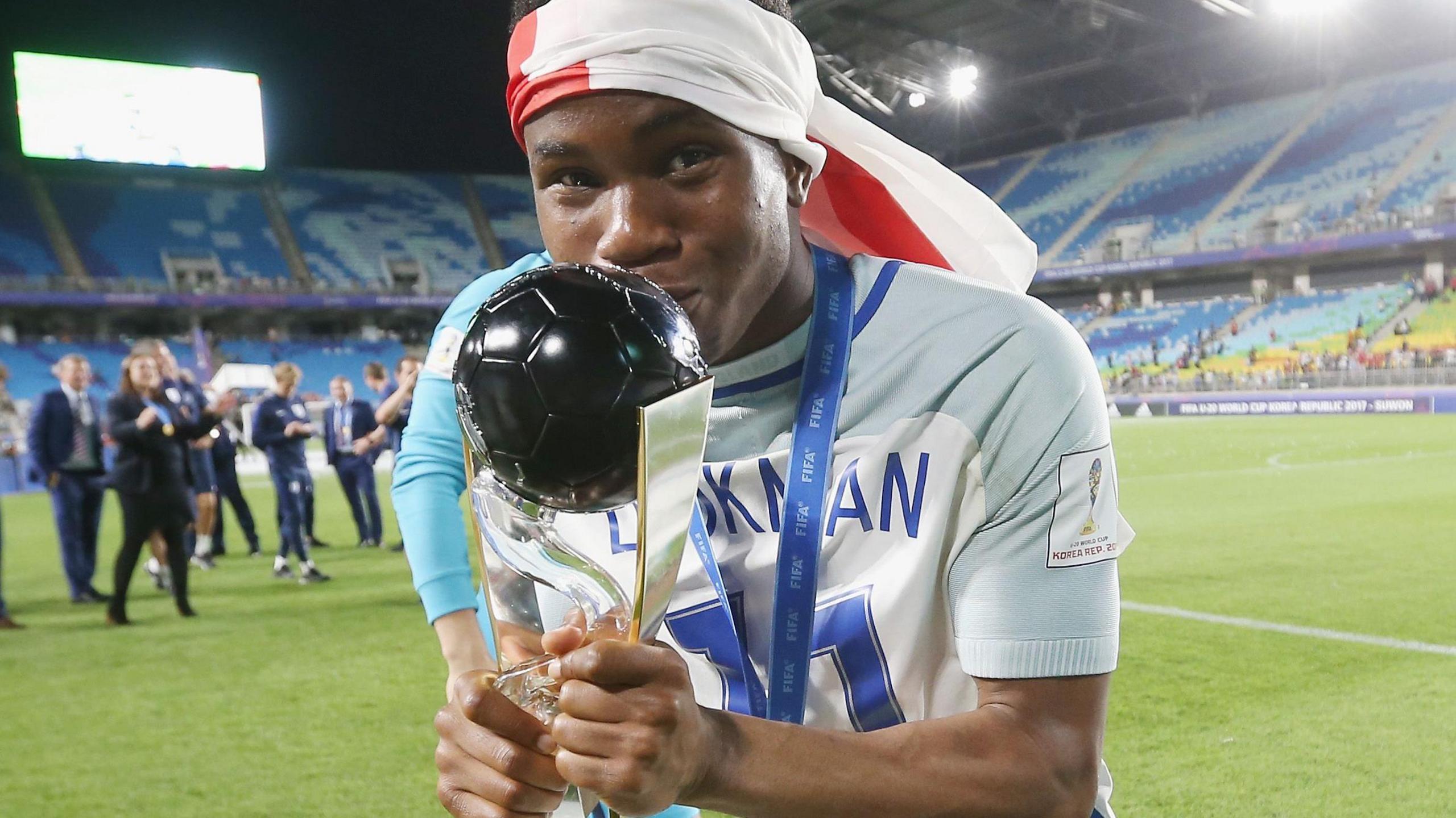 Ademola Lookman kisses the Under-20 World Cup trophy while wearing and English flag as a bandana