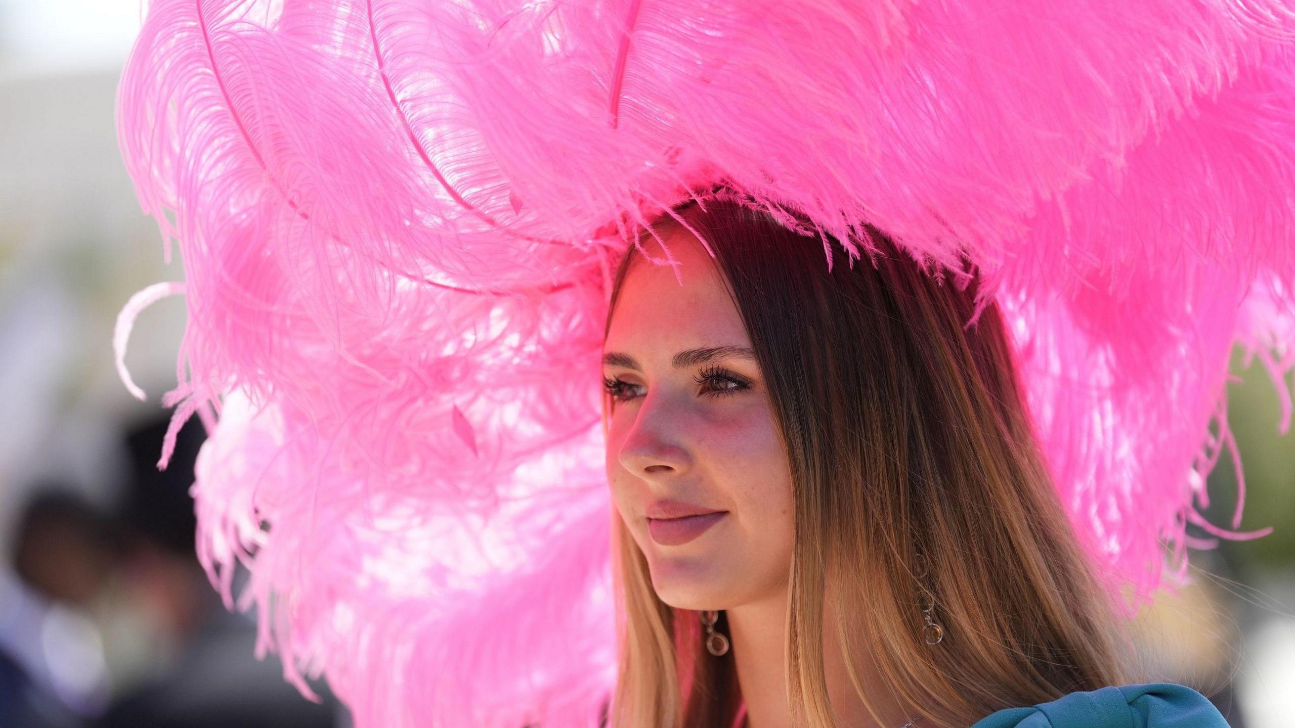 A woman wearing a large pink fascinator which is made out of feathers is smiling for the camera.