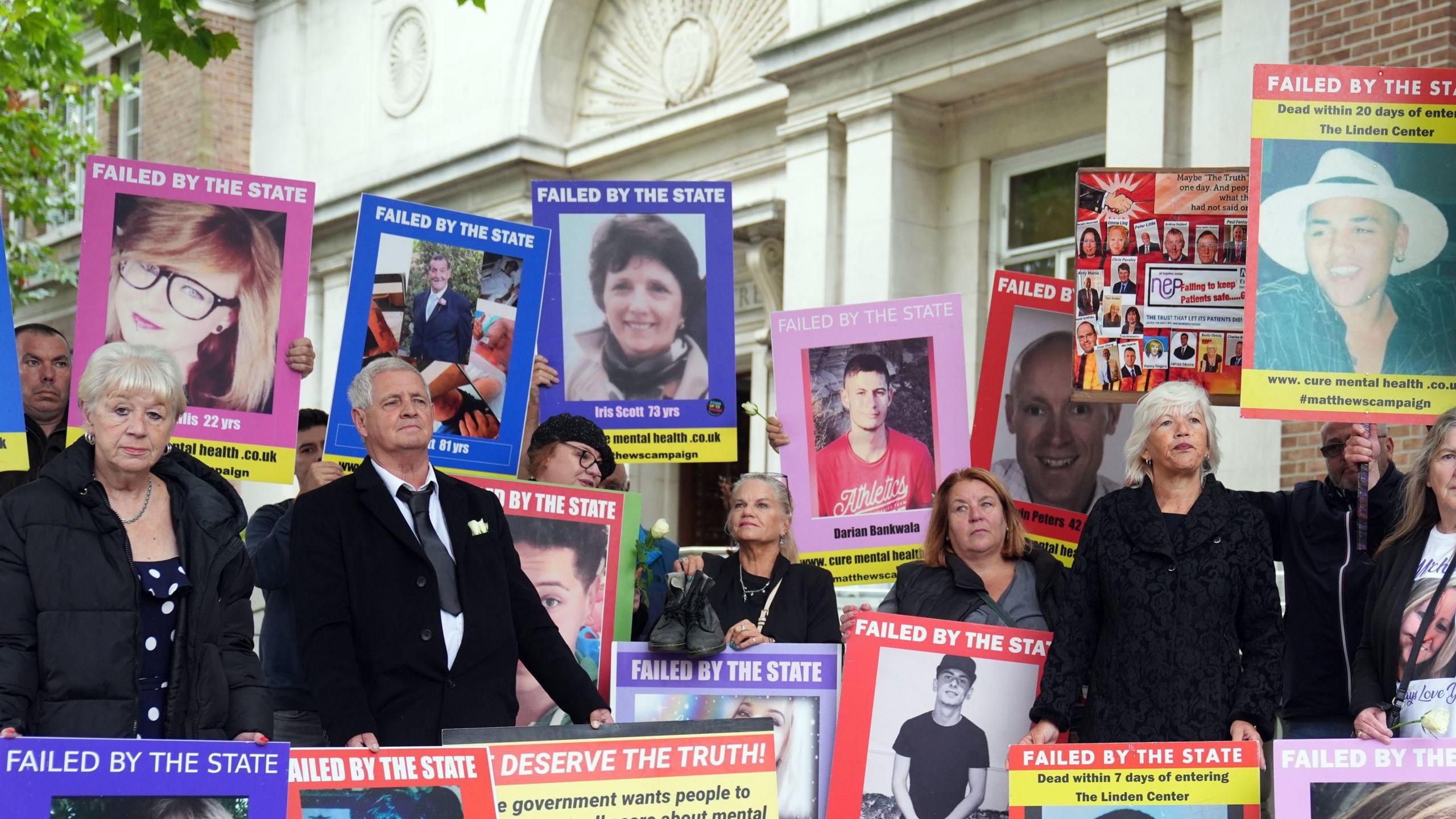The families of those who have died while in the care of mental health services in Essex stand outside the inquiry protesting. There are around 20 people in the image which shows them standing with placards held against them and large posters of their loved ones. They show a range of faces, both men and women and young and old. One reads "failed by the state".