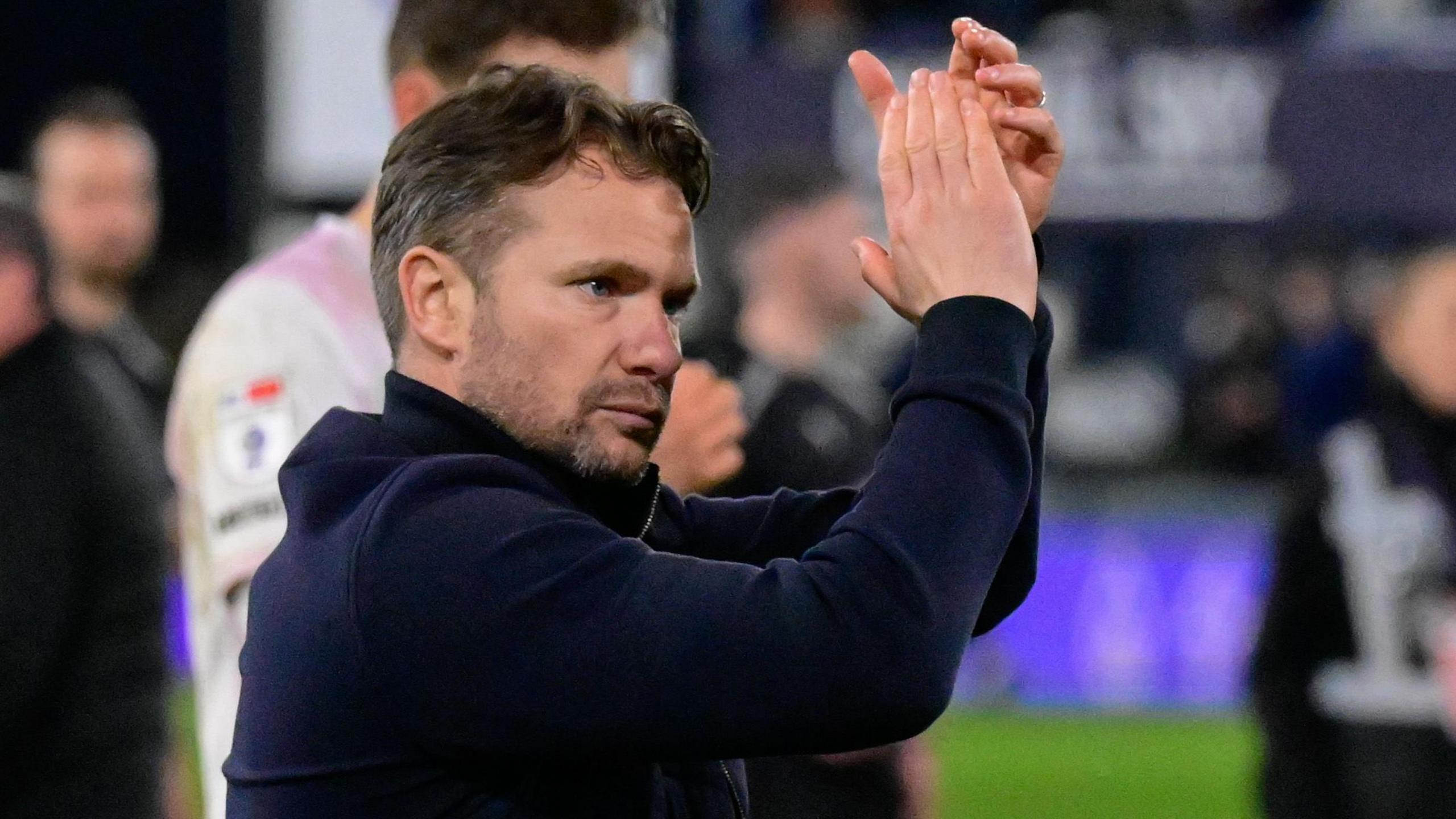 Plymouth Argyle boss Tom Cleverley, wearing a navy blue top, applauds the team's supporters