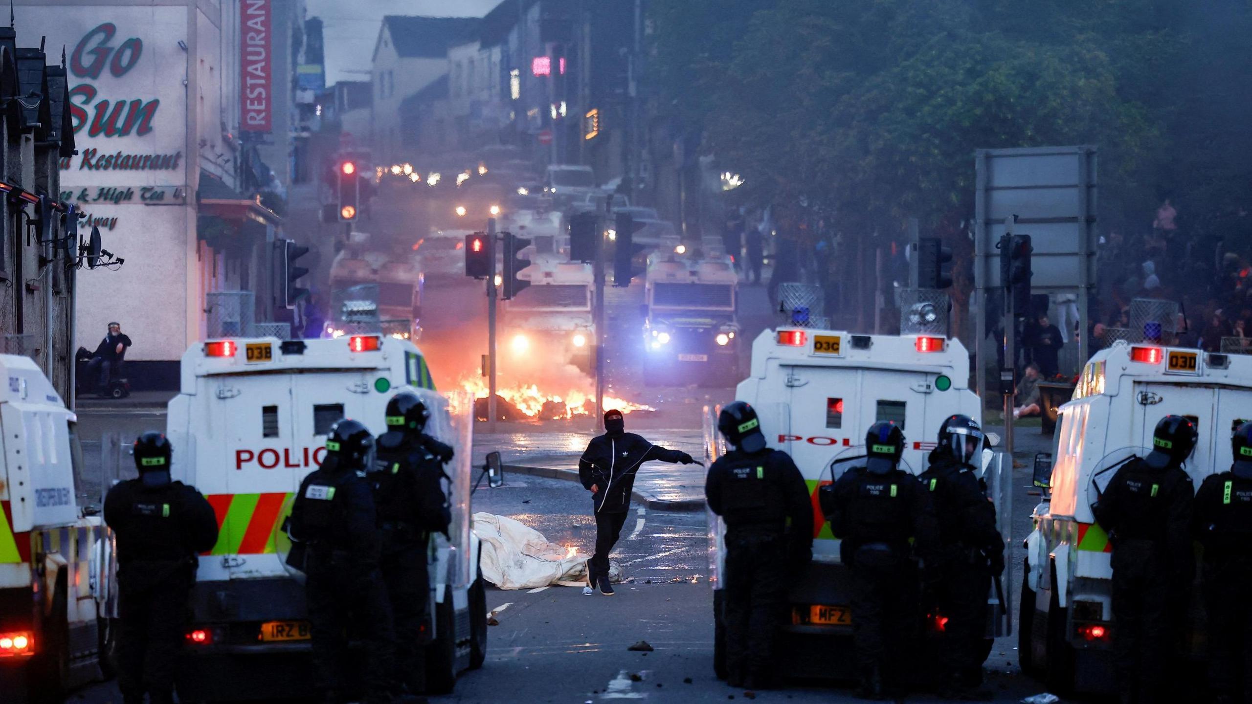 Police officers stand guard behind police vehicles during clashes on the second night of riots