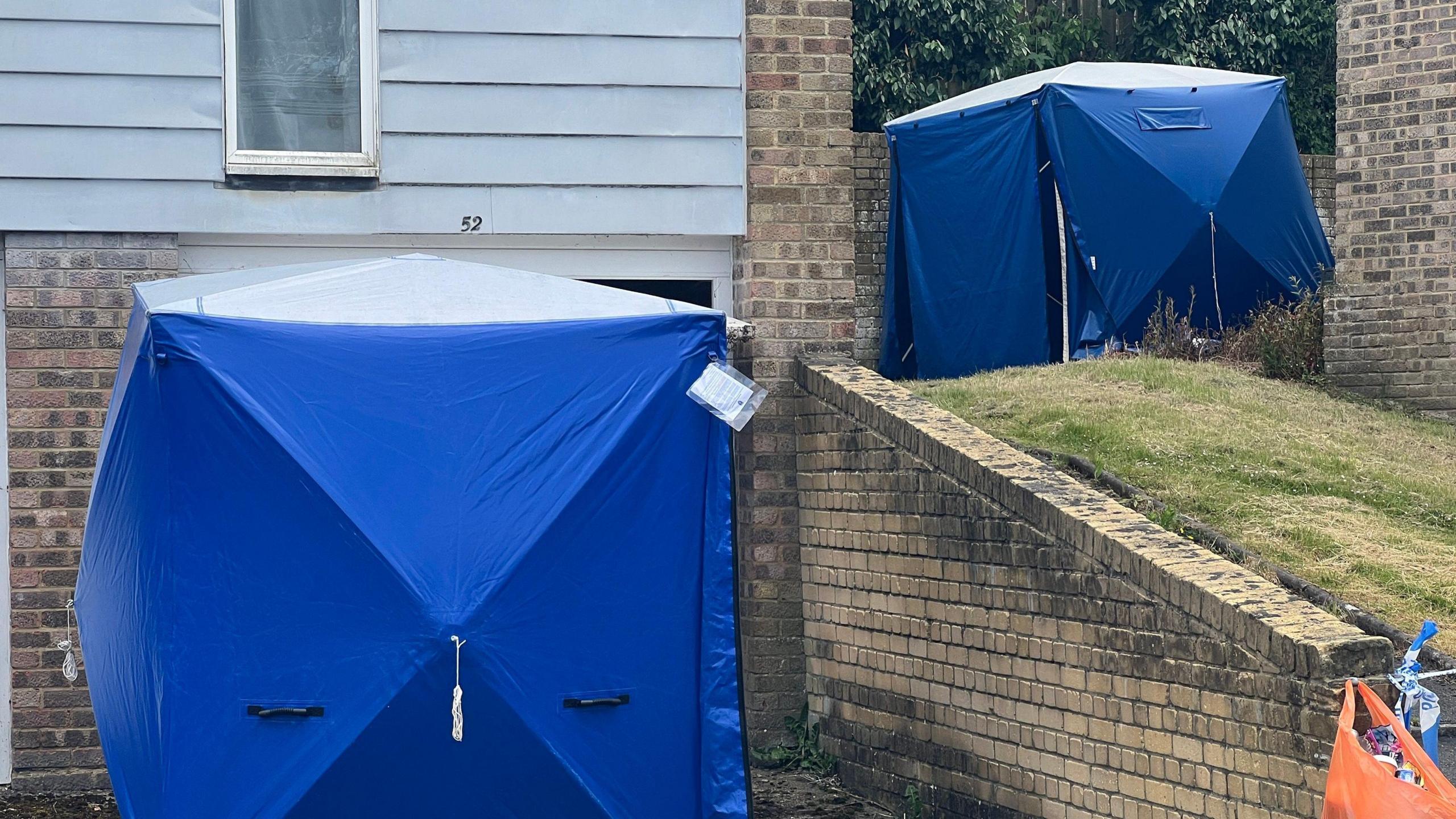 Two blue tents - one in front of a house, with one in an upper grass area - outside the Bracknell house 