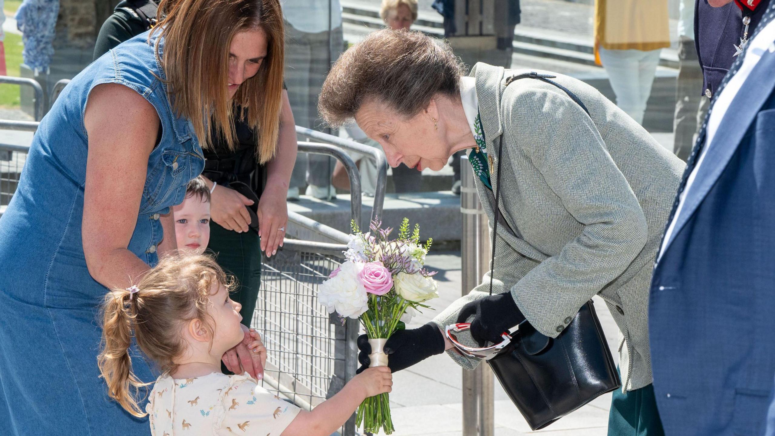 a young child presents a bouquet to a lady, while holding the hand of another woman.