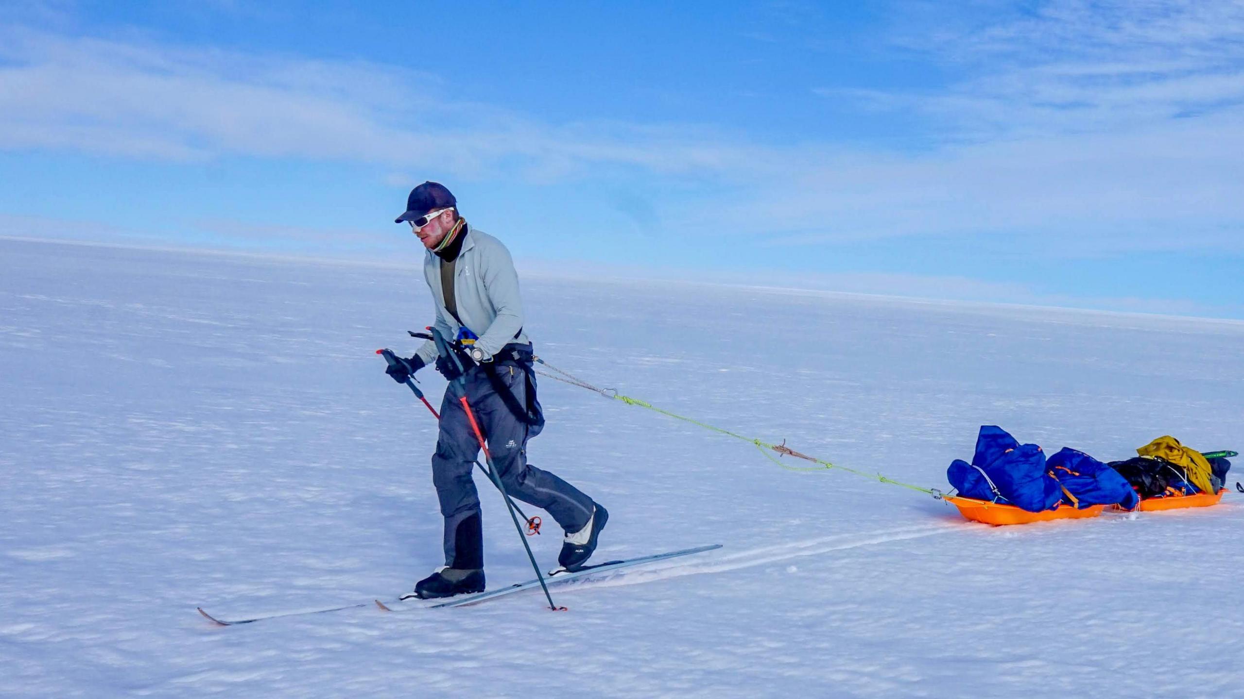 Frederick Fennessy on skis pulling a sled across snow - there is only snow and blue sky visible in the background.