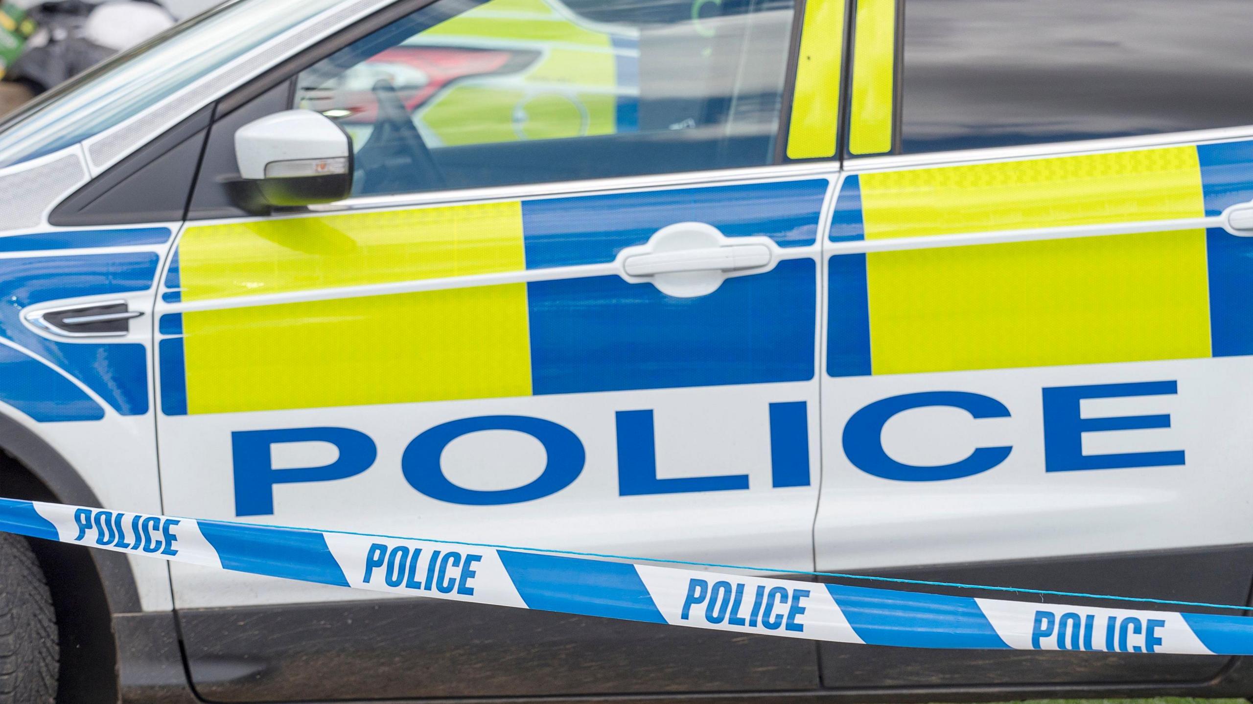 A stock image of a police car beyond blue and white police tape 