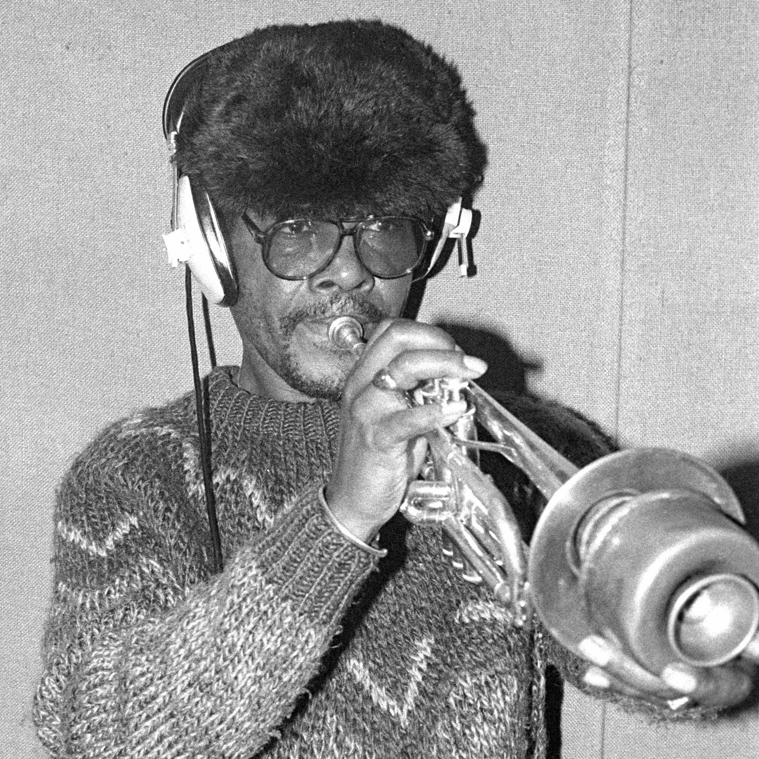 Black and white photo of Eddie 'Tan Tan' Thornton playing a trumpet while wearing headphones
