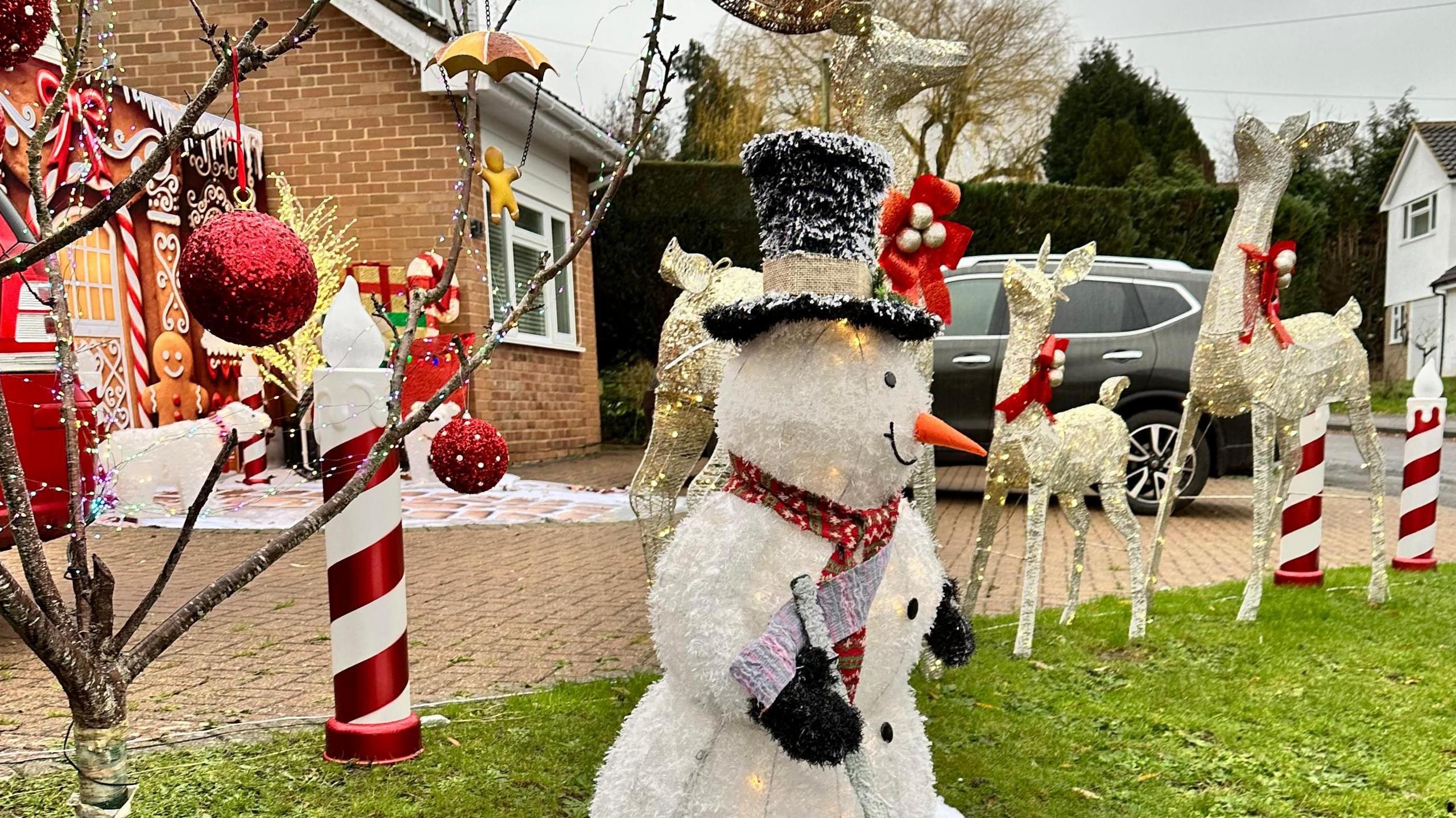 A front garden filled with a large snowman, candy canes, gingerbread men and reindeer with baubles filling a tree and a polar bear.