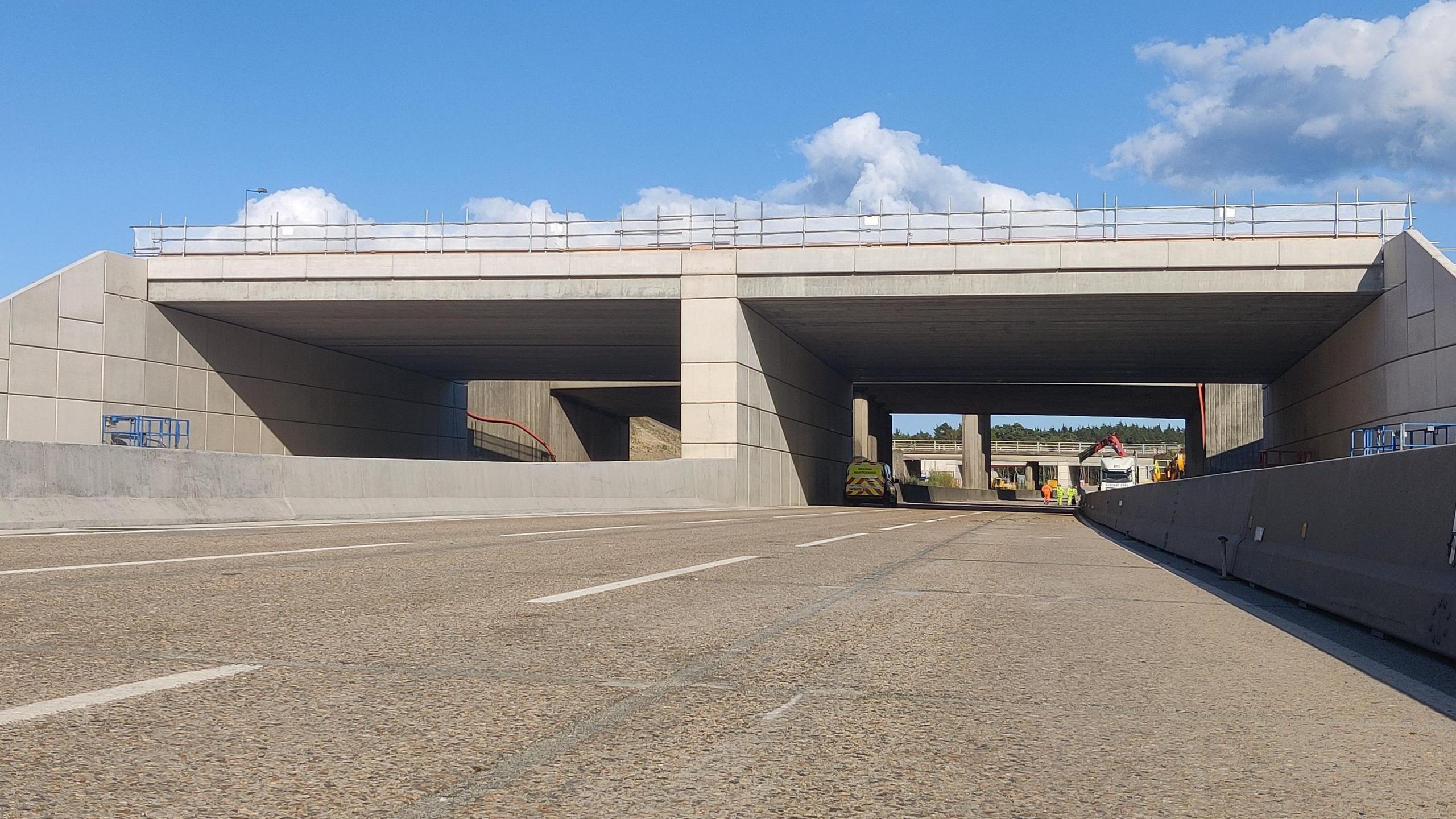 A grey concrete bridge over a deserted M25 motorway.