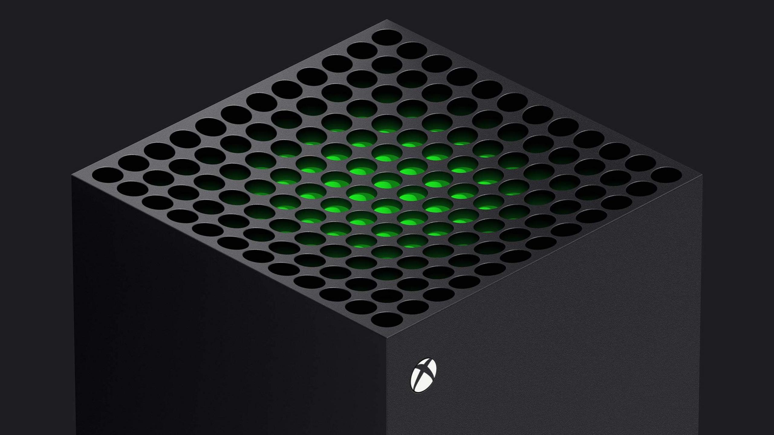 The top of a cuboid shaped Xbox One console is seen against a dark background. A green glow emanates from the circular holes on top of the machine, and a small white circle with an X inside it is printed on the side.