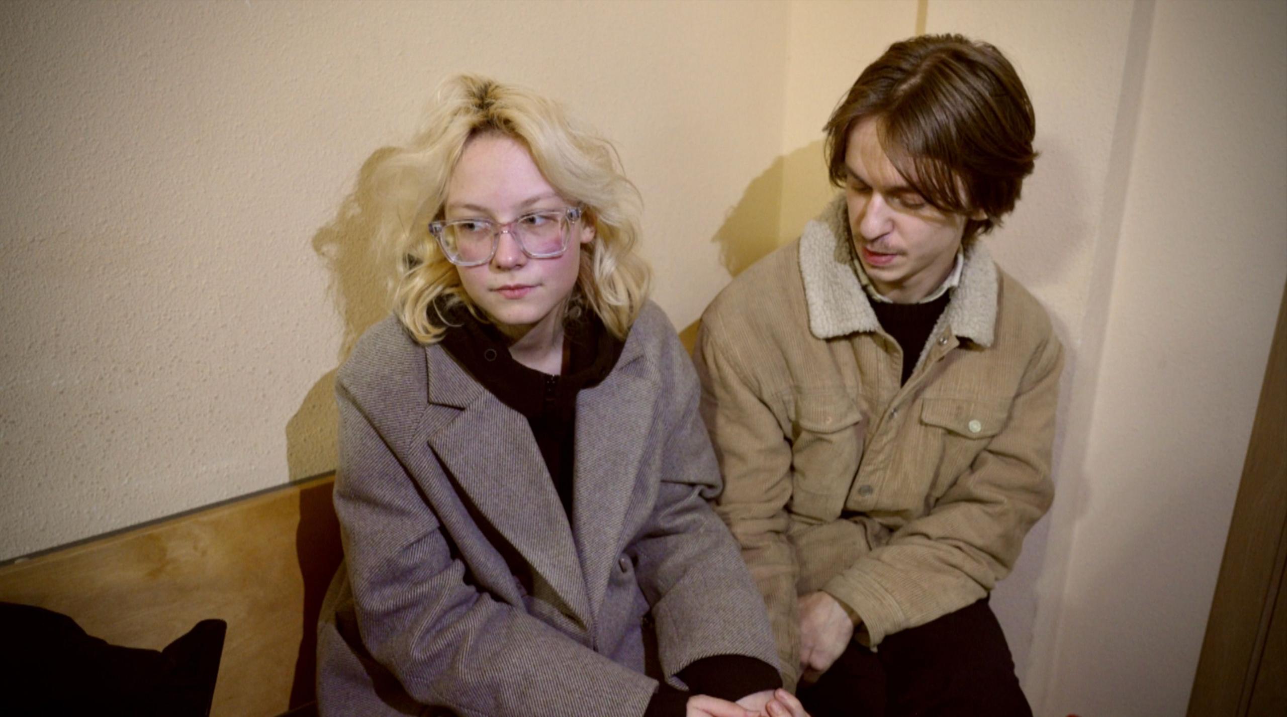Alexander Orlov (right) and Diana Loginova (left) sit holding hands on a bench in court