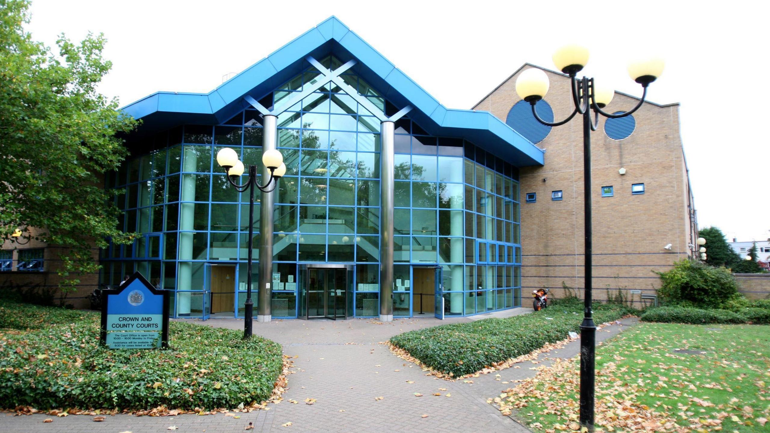 The entrance to Basildon Crown Court, which has a glass facade. Each window pane has a blue edge. The building's roof is also blue.