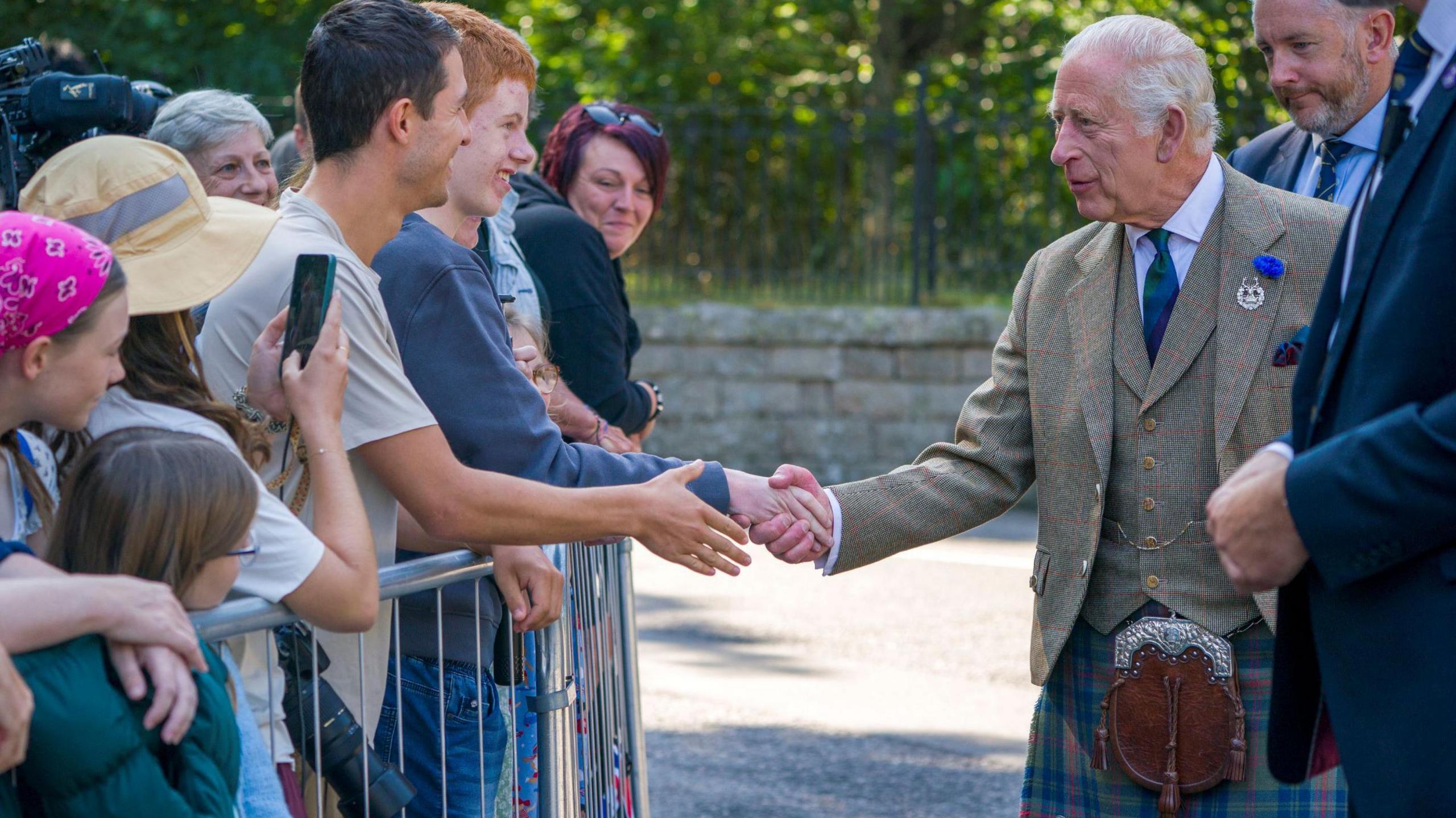 King Charles III meets members of the public after inspecting the Balaklava Company, 5th Battalion, The Royal Regiment of Scotland, at the gates of Balmoral, who are standing behind a metal barrier.