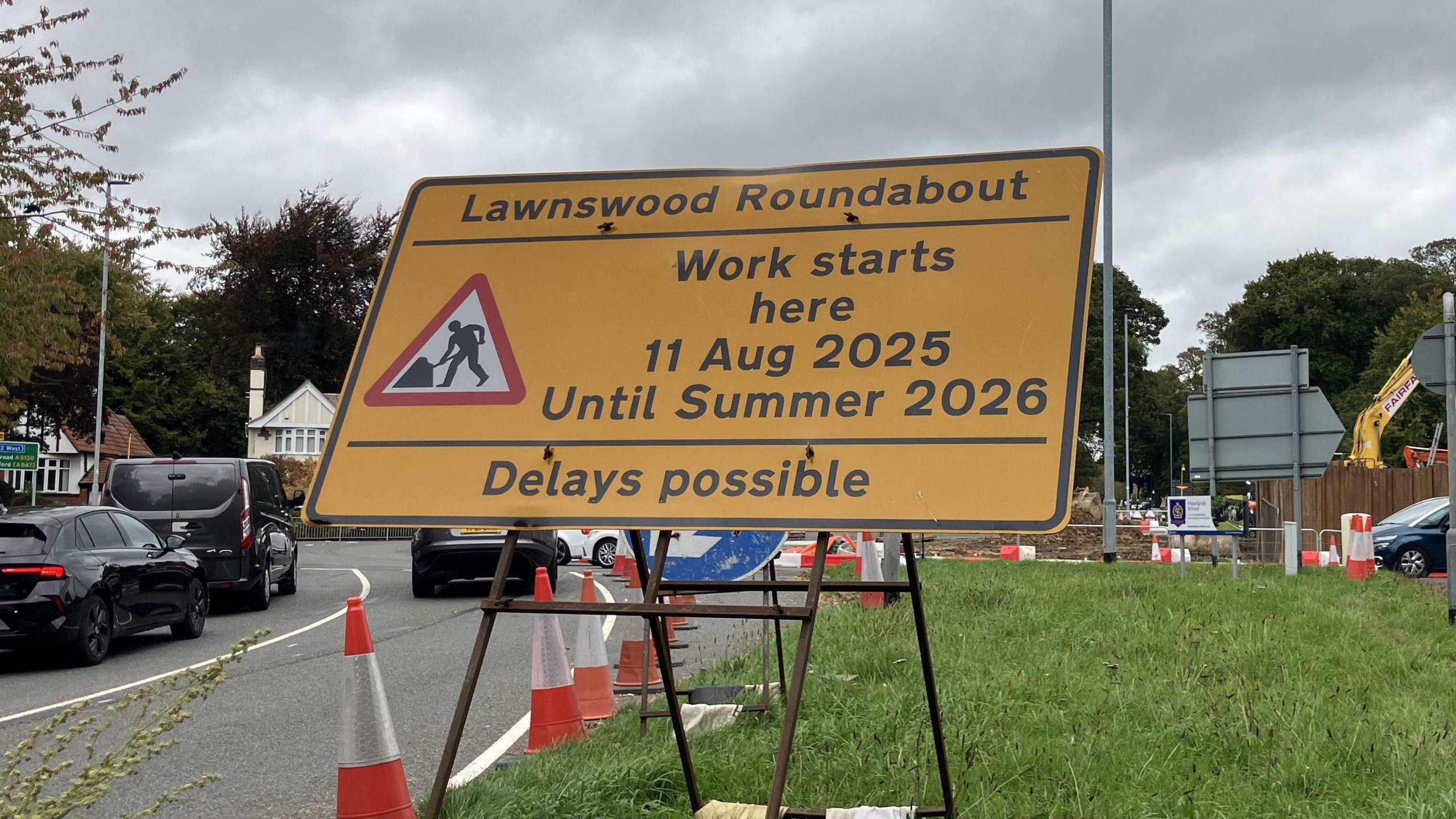 A yellow sign showing that construction work will be taking place, with construction happening in the background.