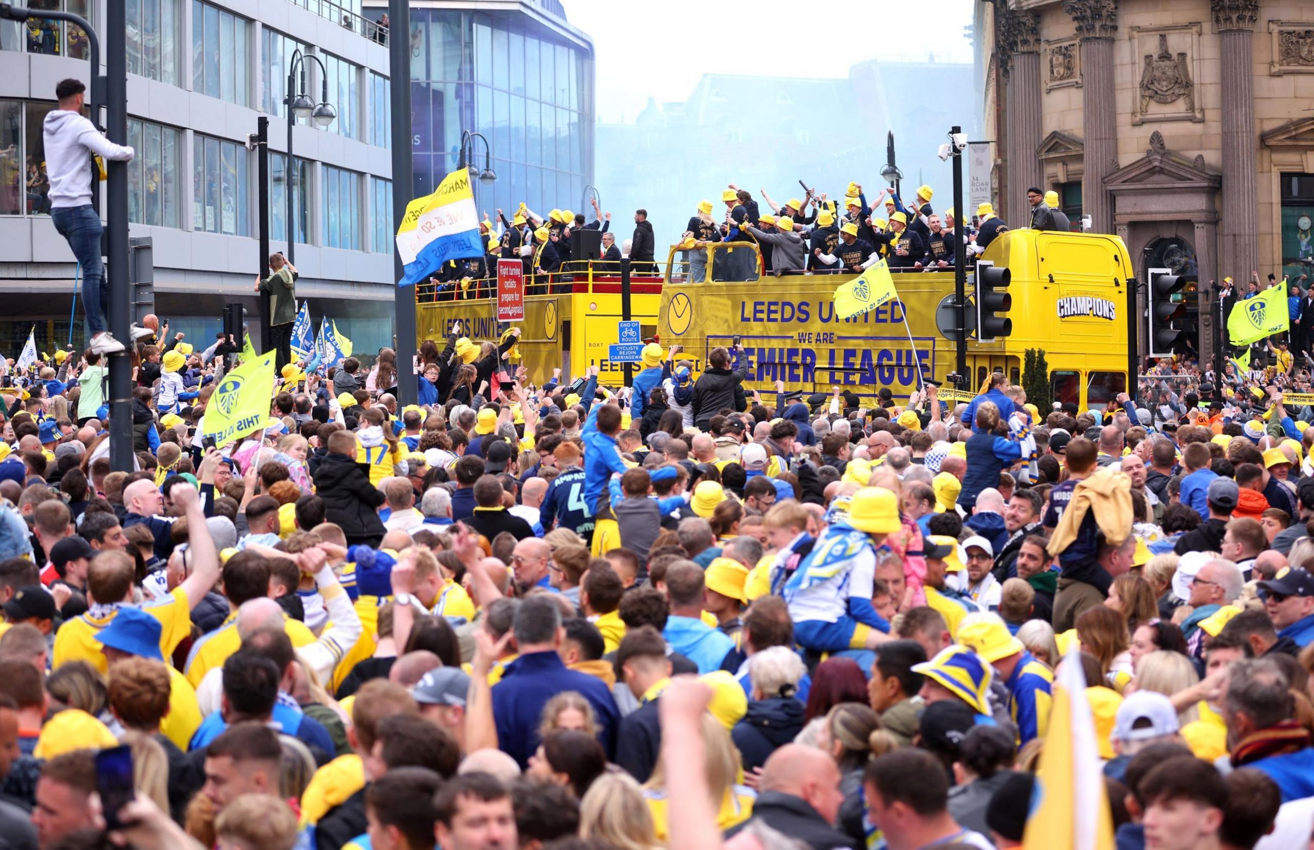 Hundreds of fans wave flags and watch the Leeds United bus in the background 