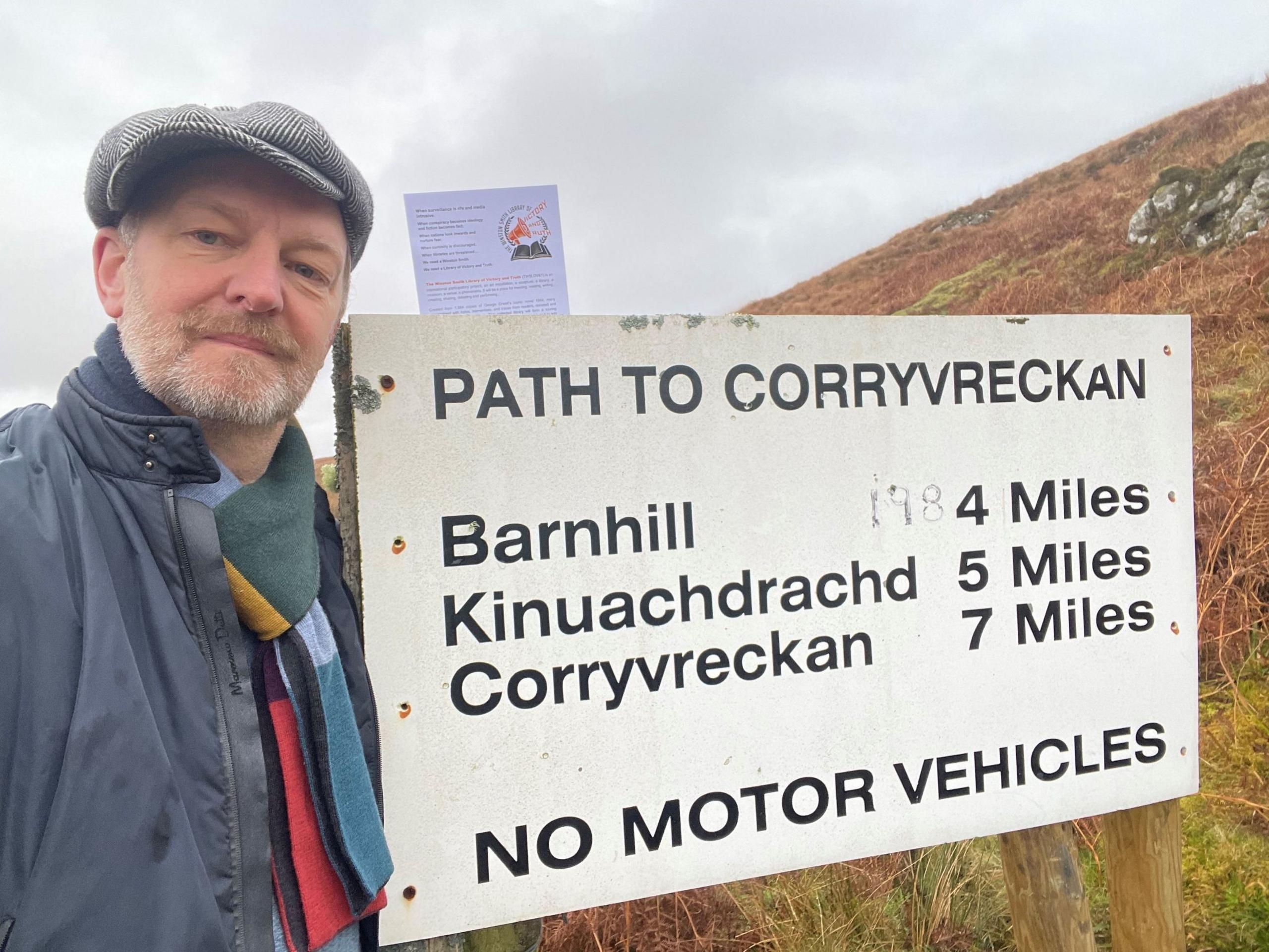 Mr Clausen poses beside a road sign on Jura indicating four miles to Barnhill