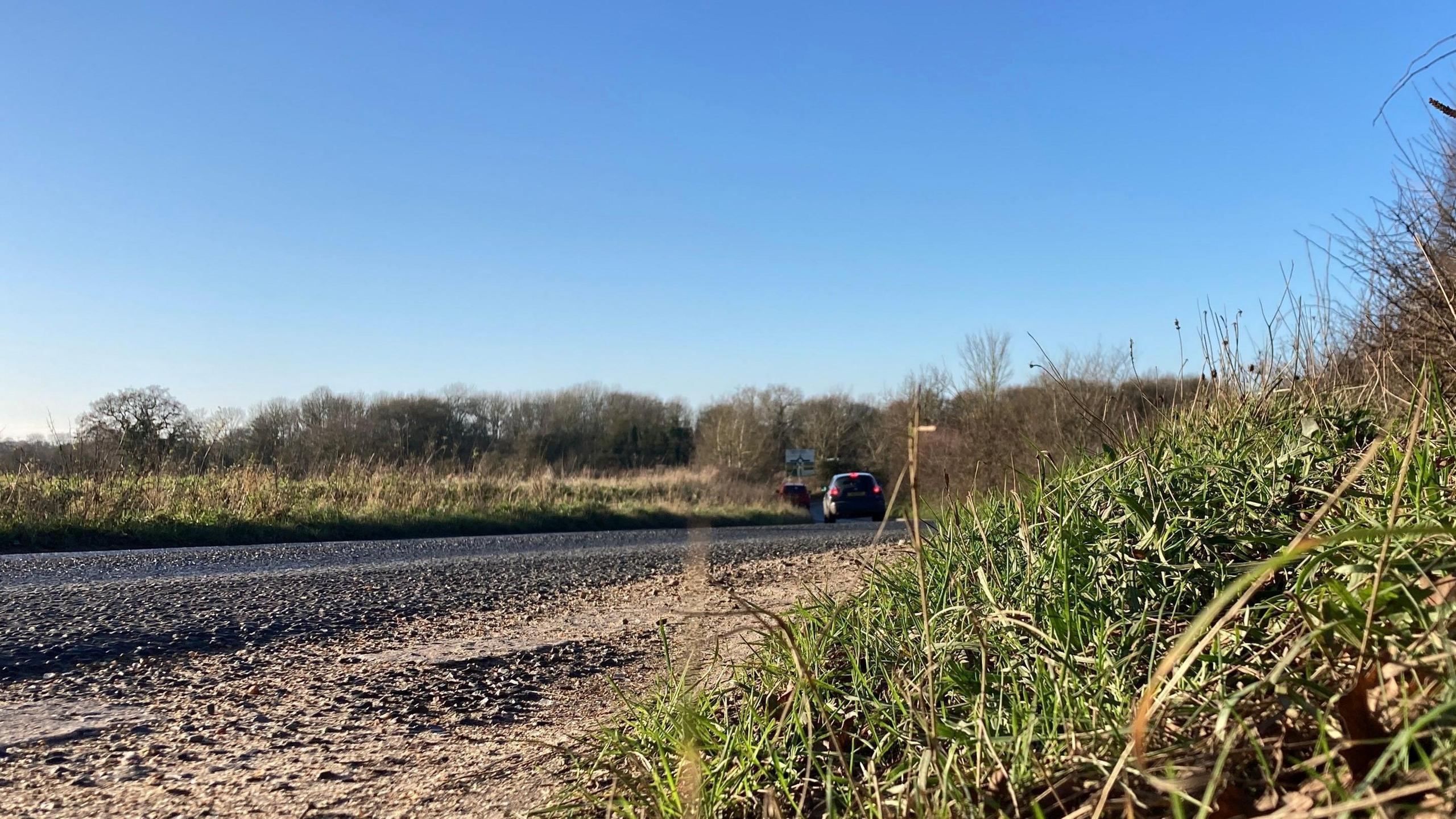 A car travelling along Tivetshall Road. It is a rural road with grass banks either side