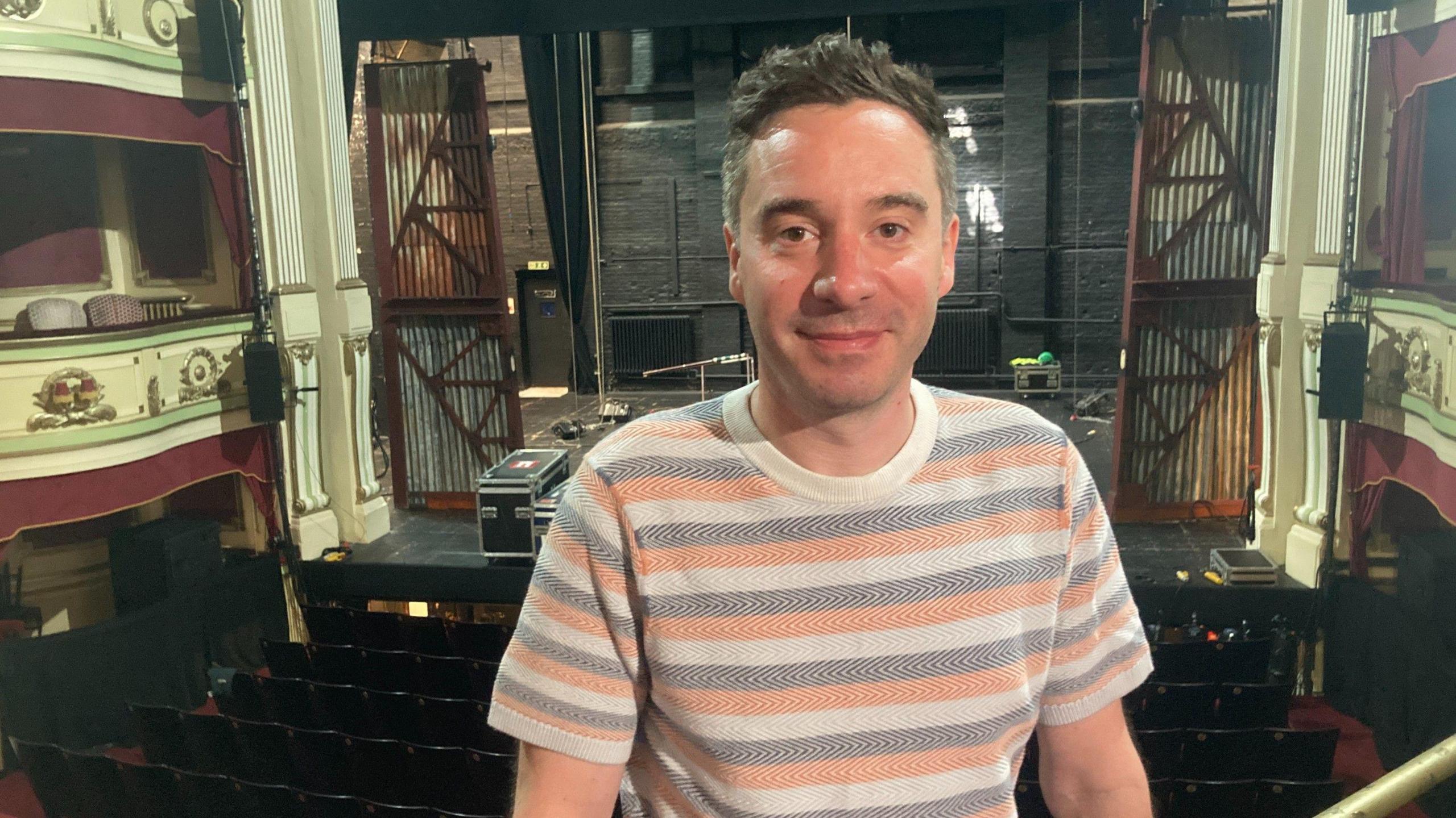 James Graham, wearing a striped t-shirt, sits in the stalls of the Theatre Royal, Brighton, with his back to the stage.