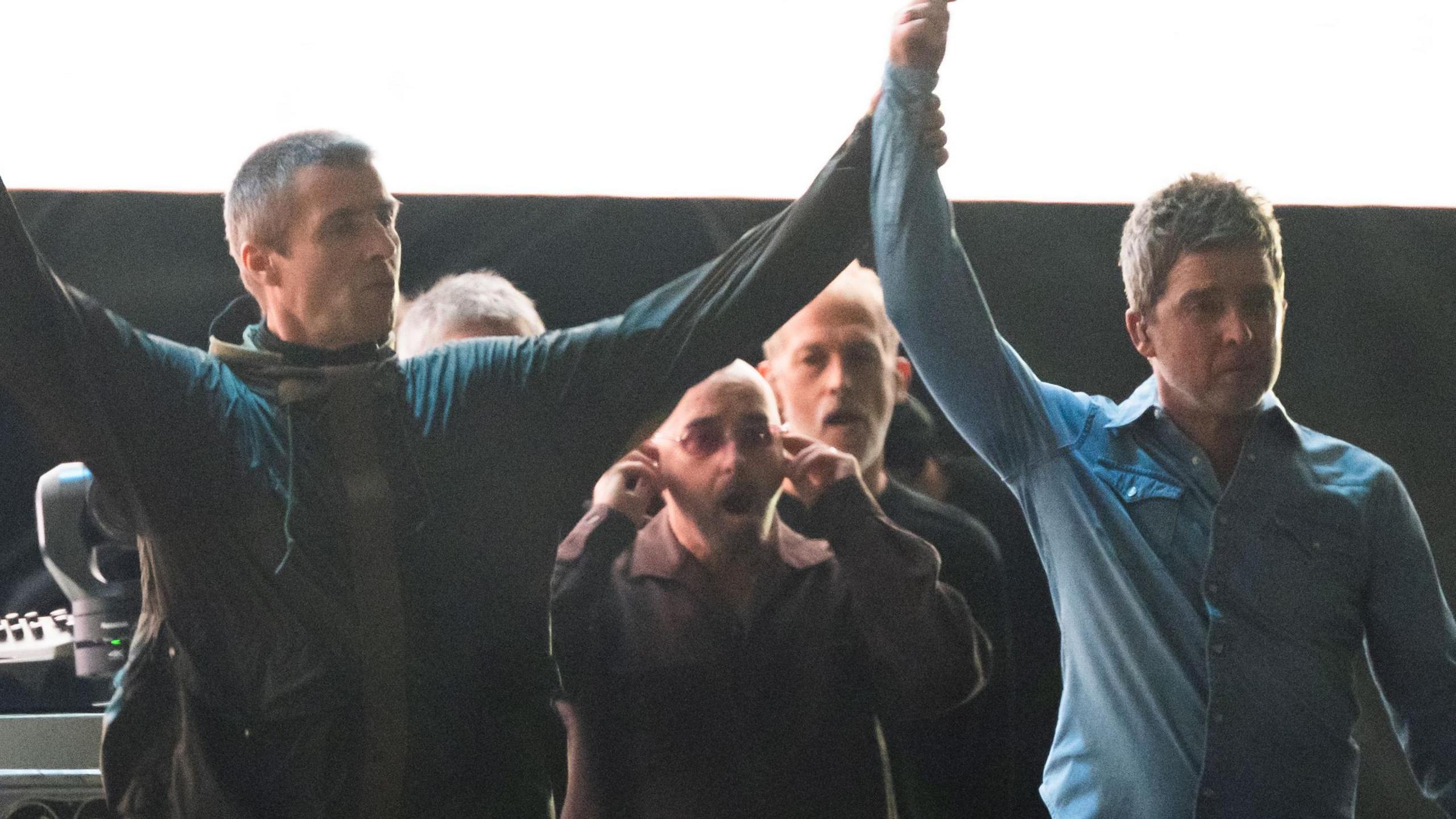Liam and Noel Gallagher with their arms raised aloft together while walking on-stage at their first comeback gig in Cardiff in July