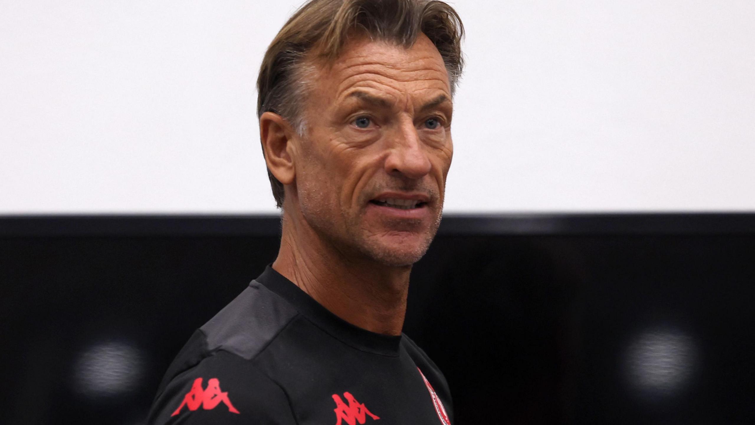 Herve Renard, visible from shoulders up, wears a wearing a black Tunisia training top as he looks over his right shoulder towards the camera