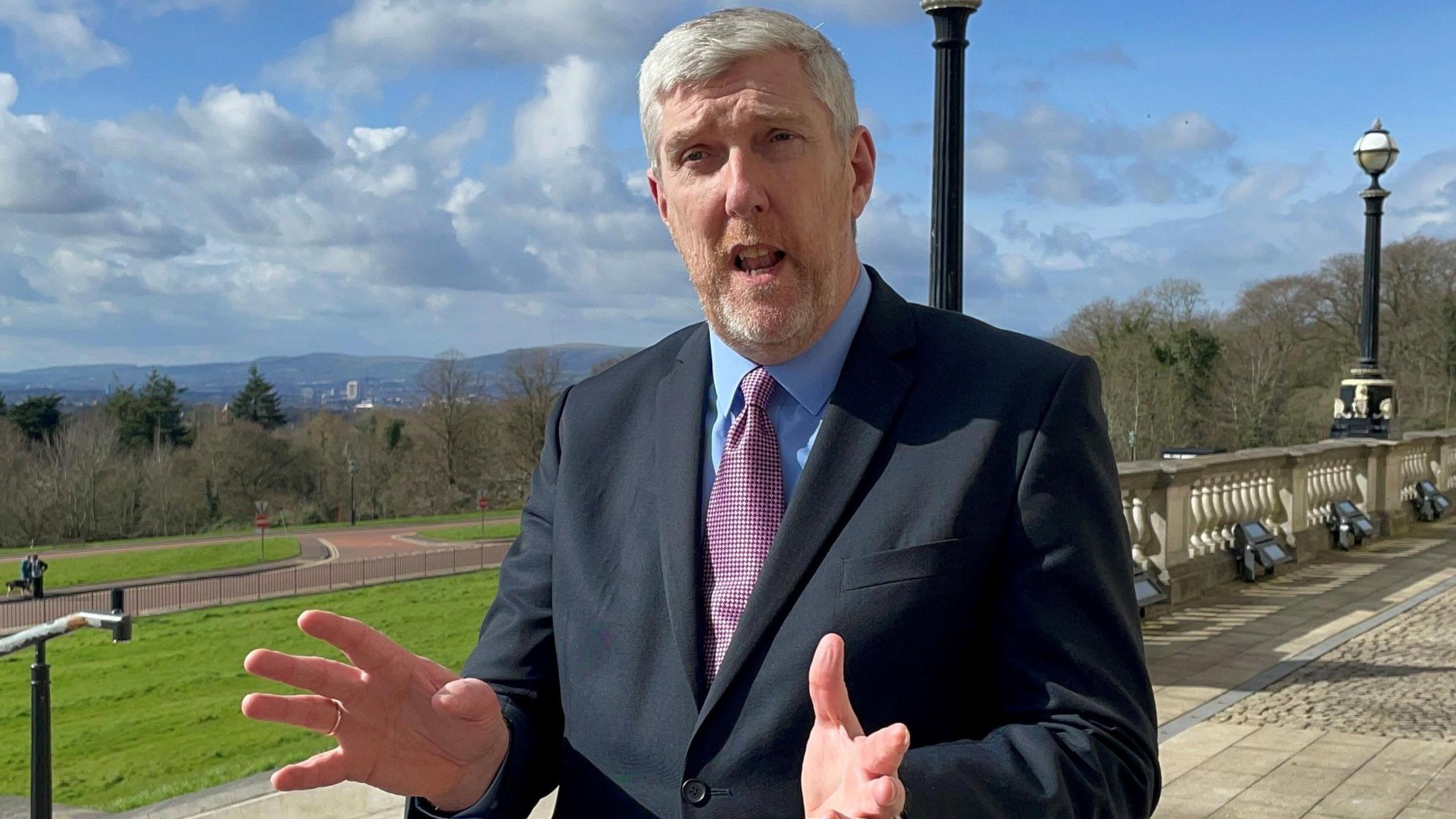 A man wearing a dark suit stood in front of parliament buildings in Belfast