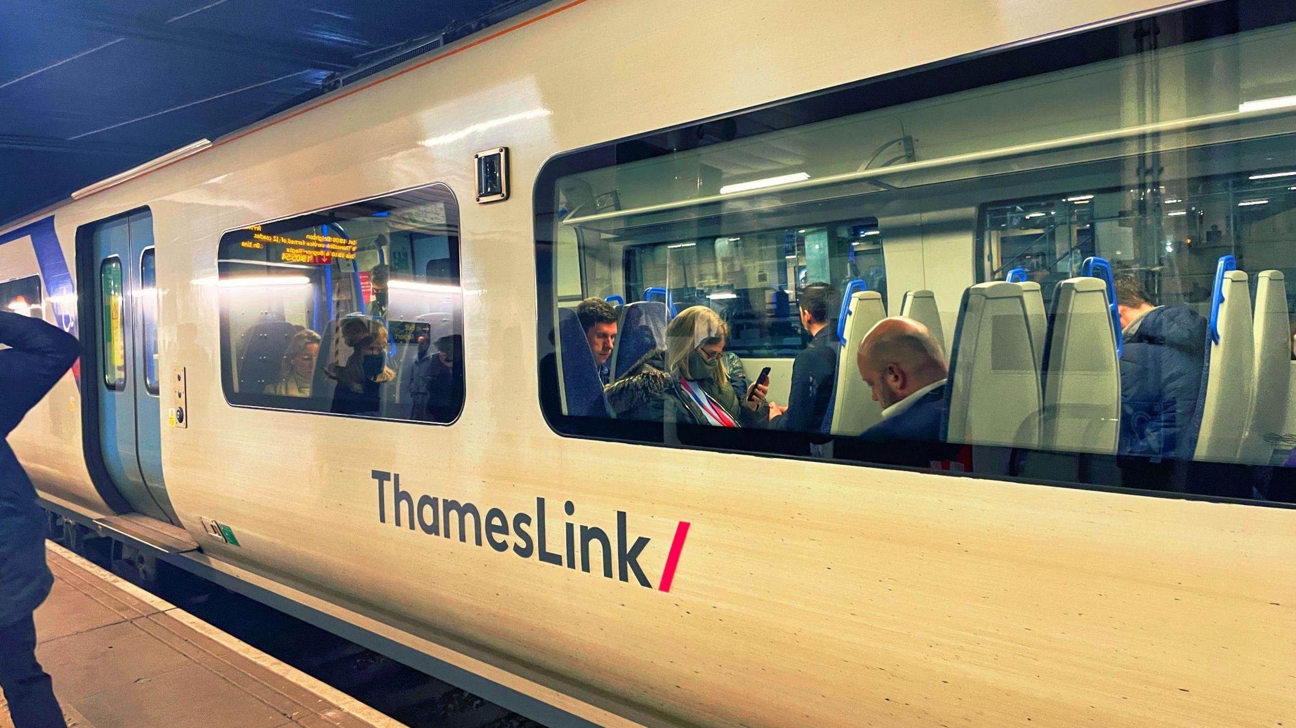 Passengers sit aboard a white and blue liveried Thameslink train.