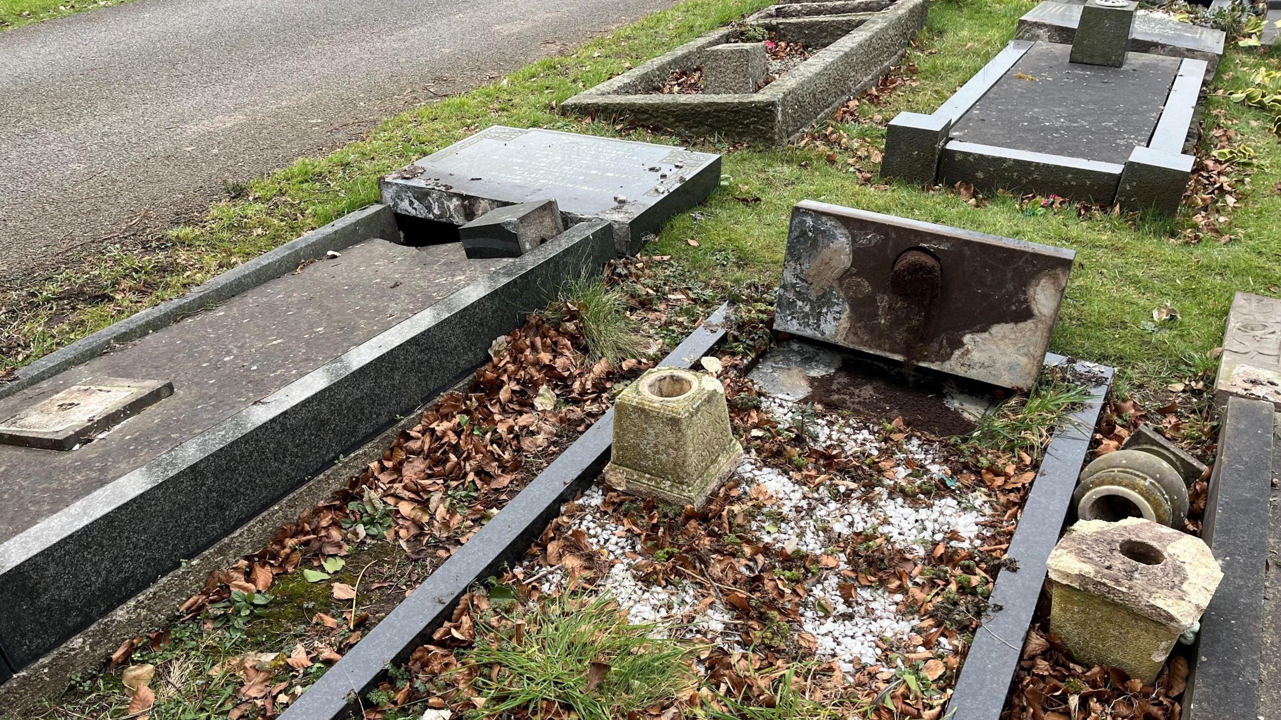 Several grave headstones uprooted from the ground, knocked over on to the grass.